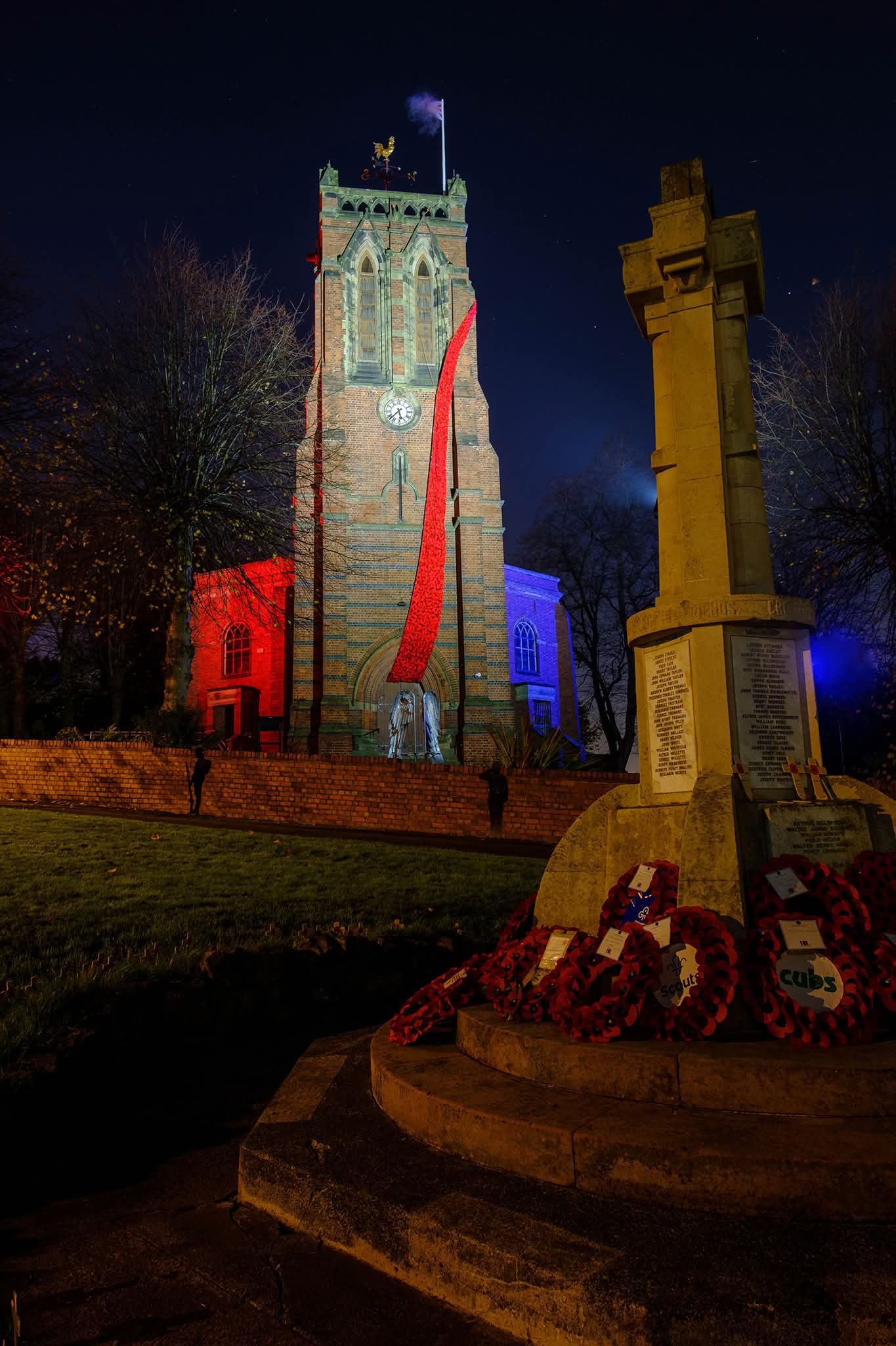 Poppies cascading down Cradley Church lit up at night with the war memorial in the foreground