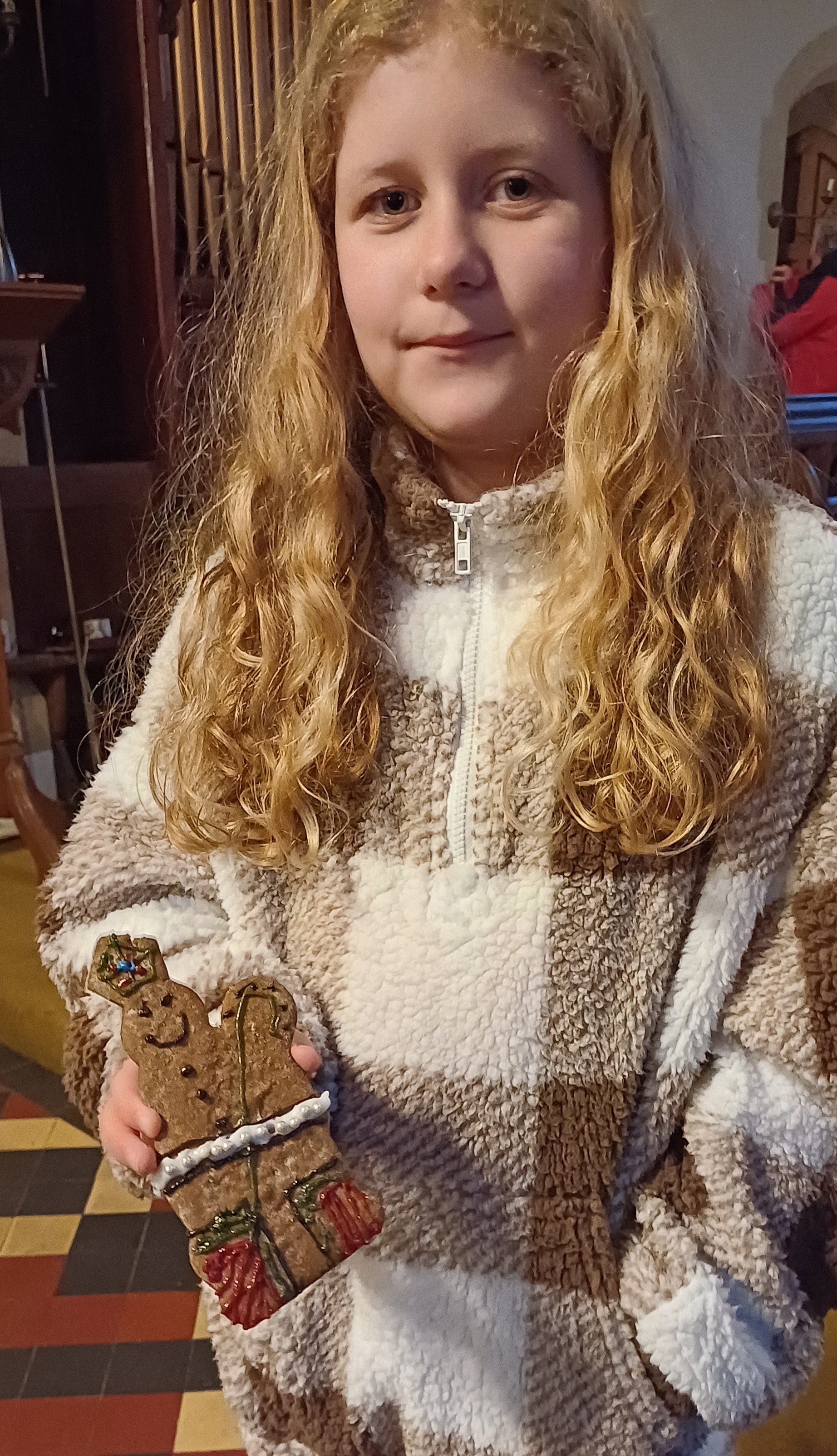 A girl holding a biscuit shaped like St Nicholas which she has decorated