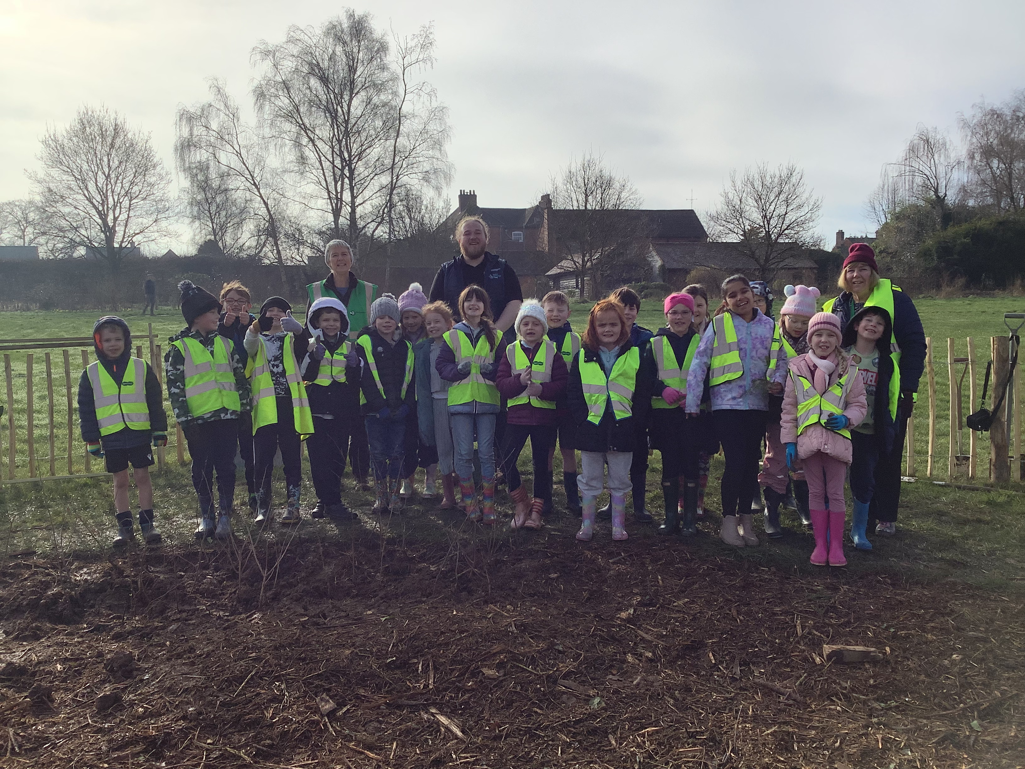 Children from Hindlip first school in hi-vis jackets standing next to the meadow where they are planting trees