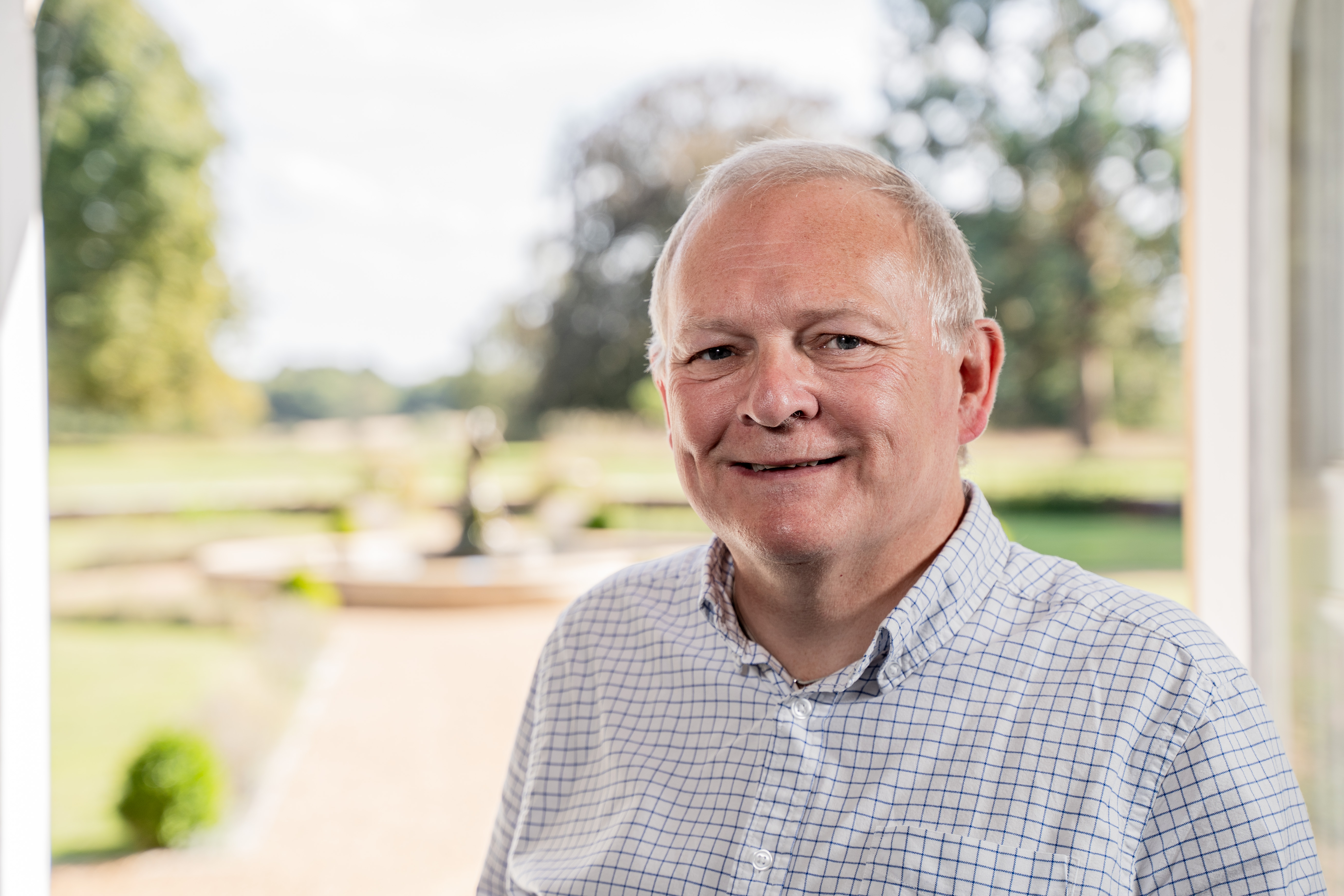 Head and shoulder shot of Tim Williams standing in front of a garden.