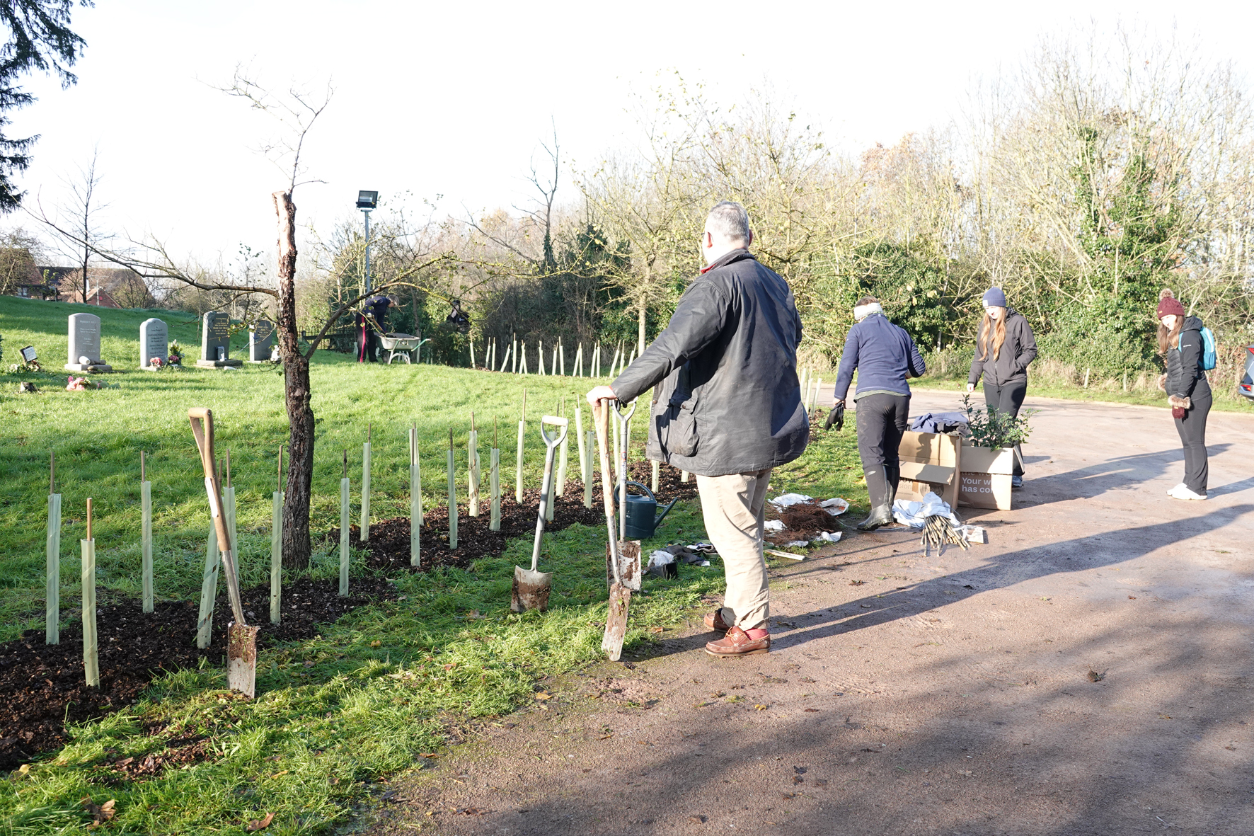 People helping to plant a hedge at the edge of a churchyard