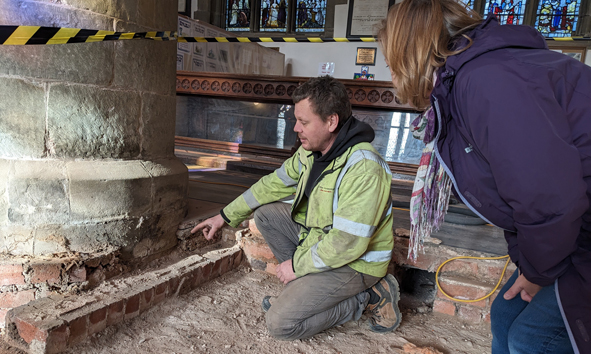 Two people looking at the uncovered base of the stone pillars in Malvern Priory