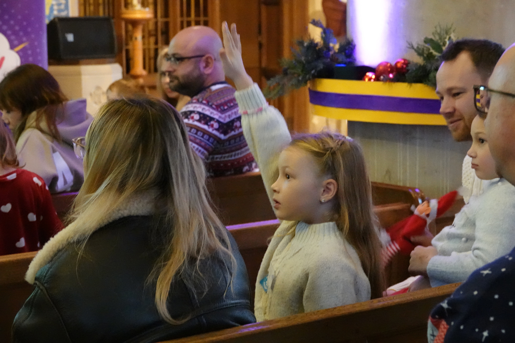 A girl sat in a pew surrounded by adults with her hand in the aid