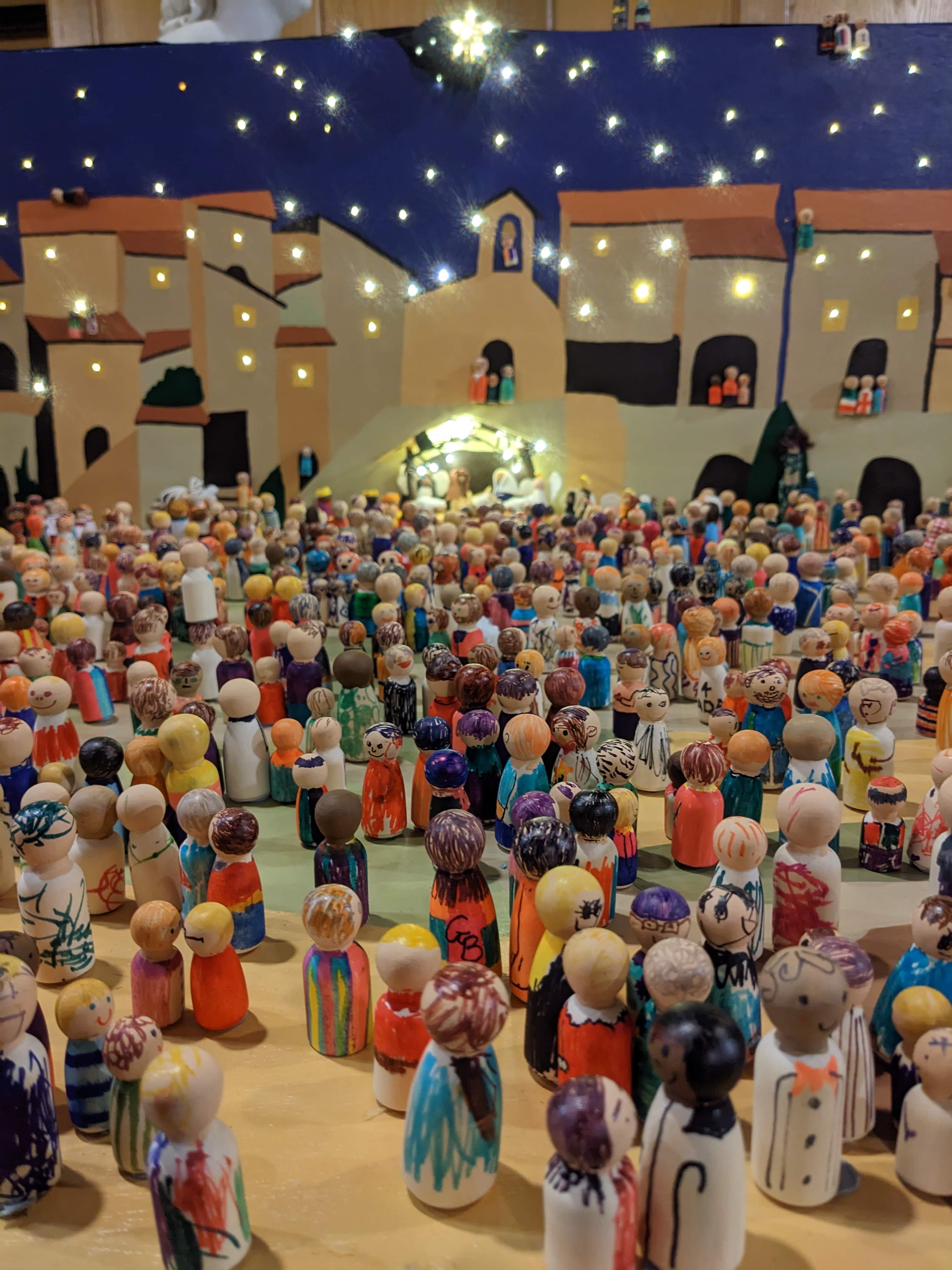 A close up of the peg doll nativity with the scenery lit up in the background