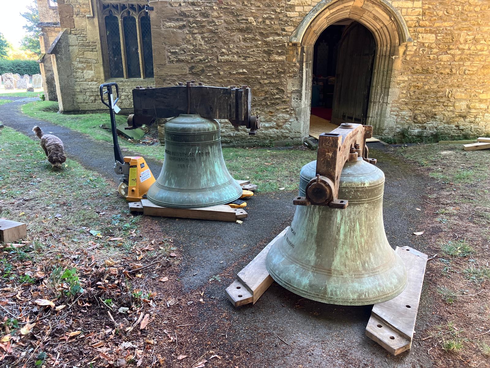 Two old bells sitting on wooden panels outside Elmley Castle church