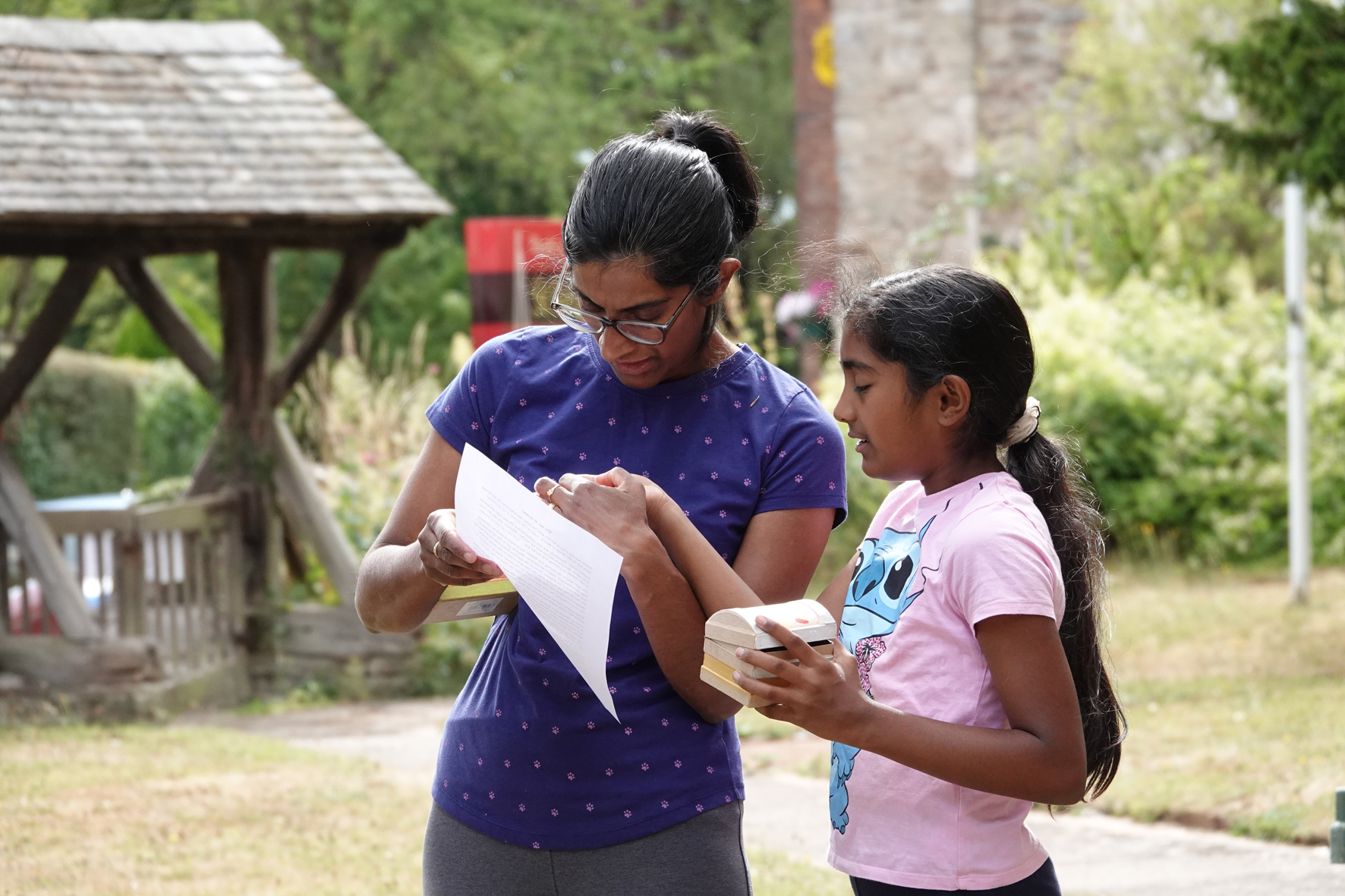 A mother and her daughter look together at a sheet of paper while holding small treasure boxes