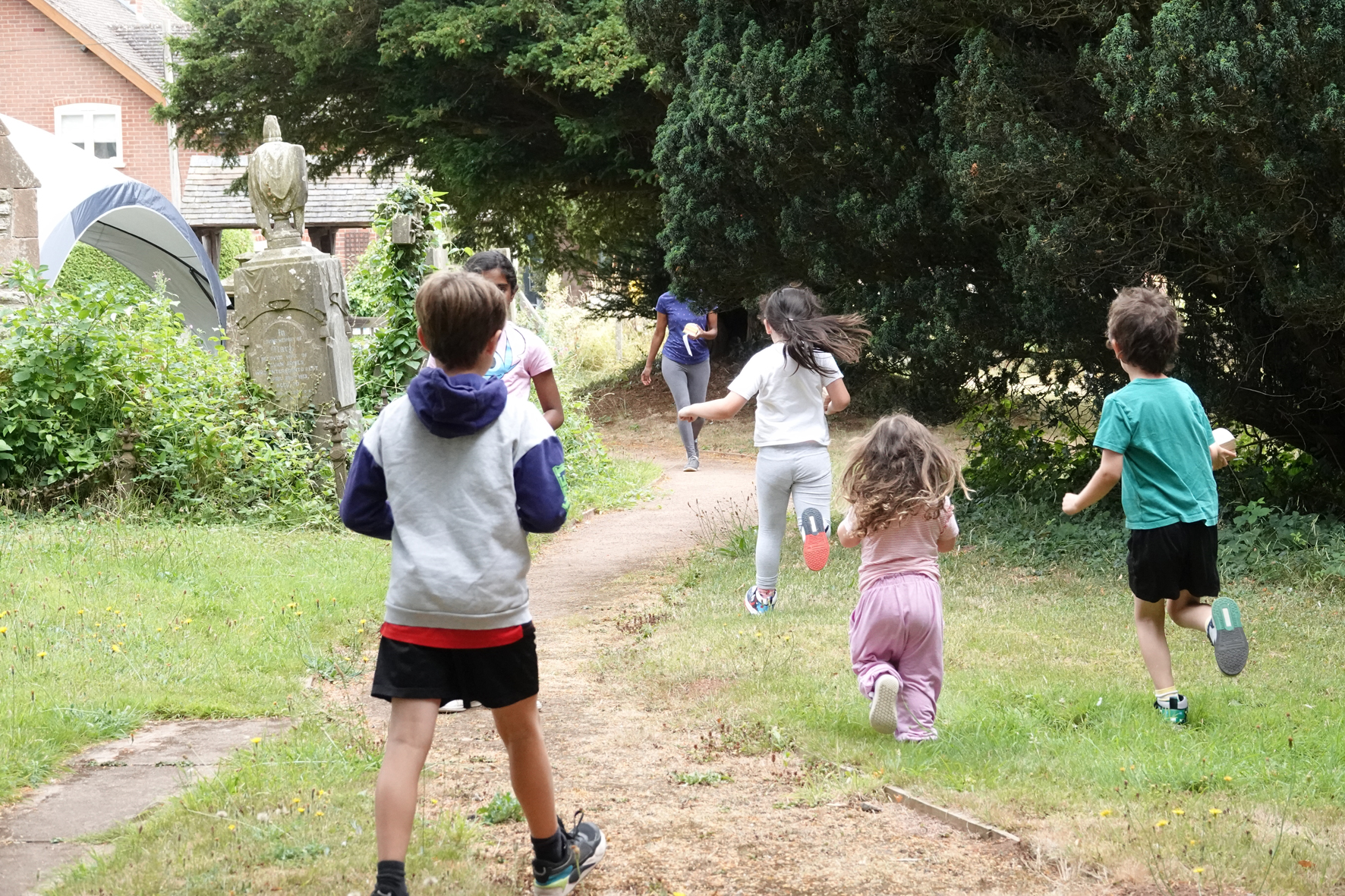 Children run down the path away from the camera at Clifton on Teme churchyard
