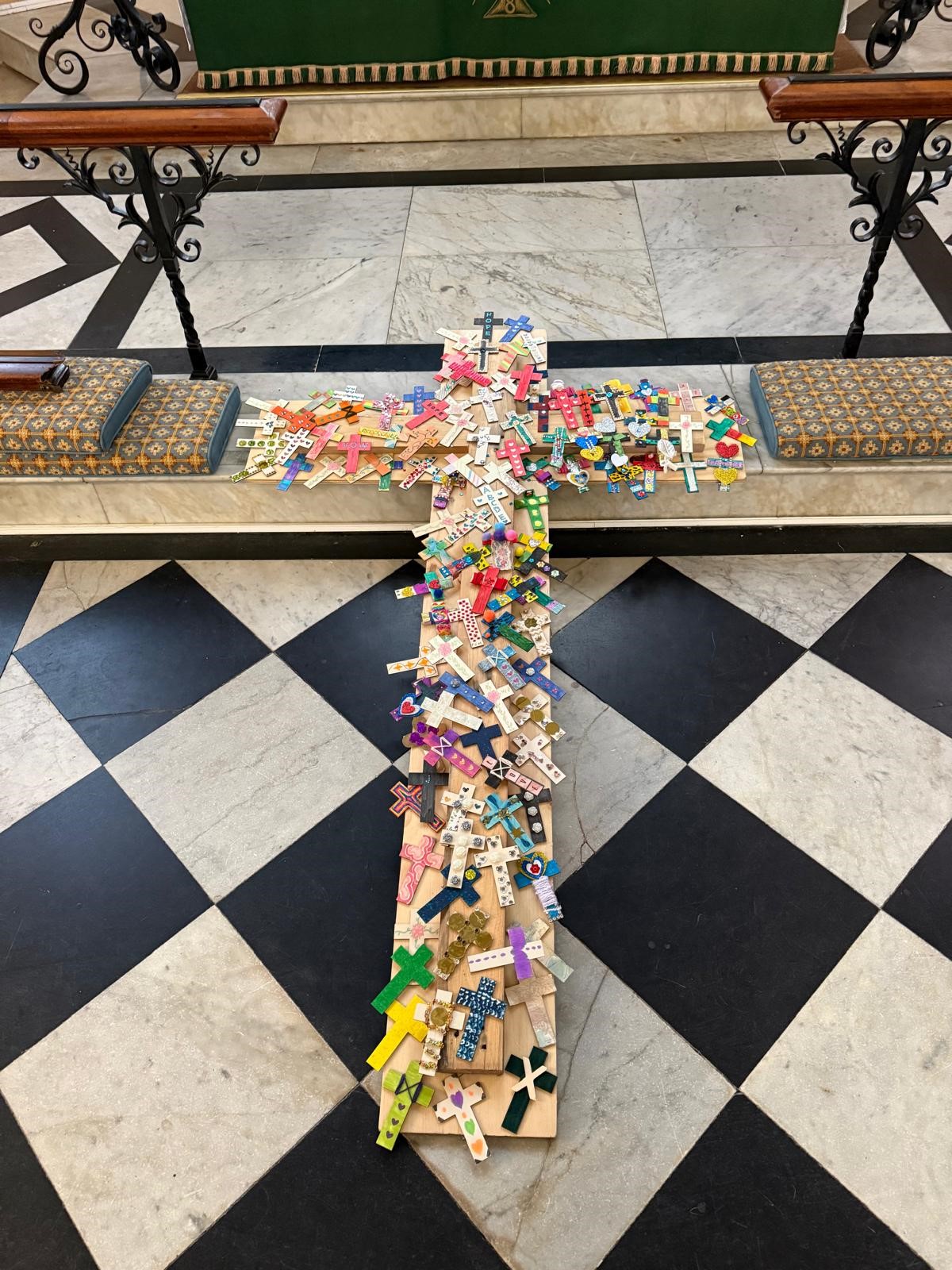 A wooden cross covered in decorated small crosses on the floor of the church in front of the altar