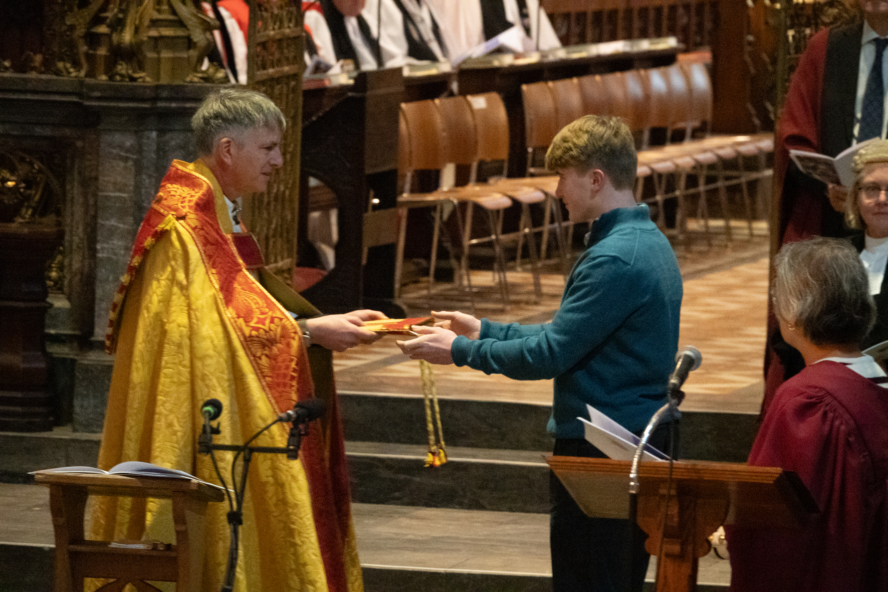 A young person hands over Bishop Hugh's mitre to him.