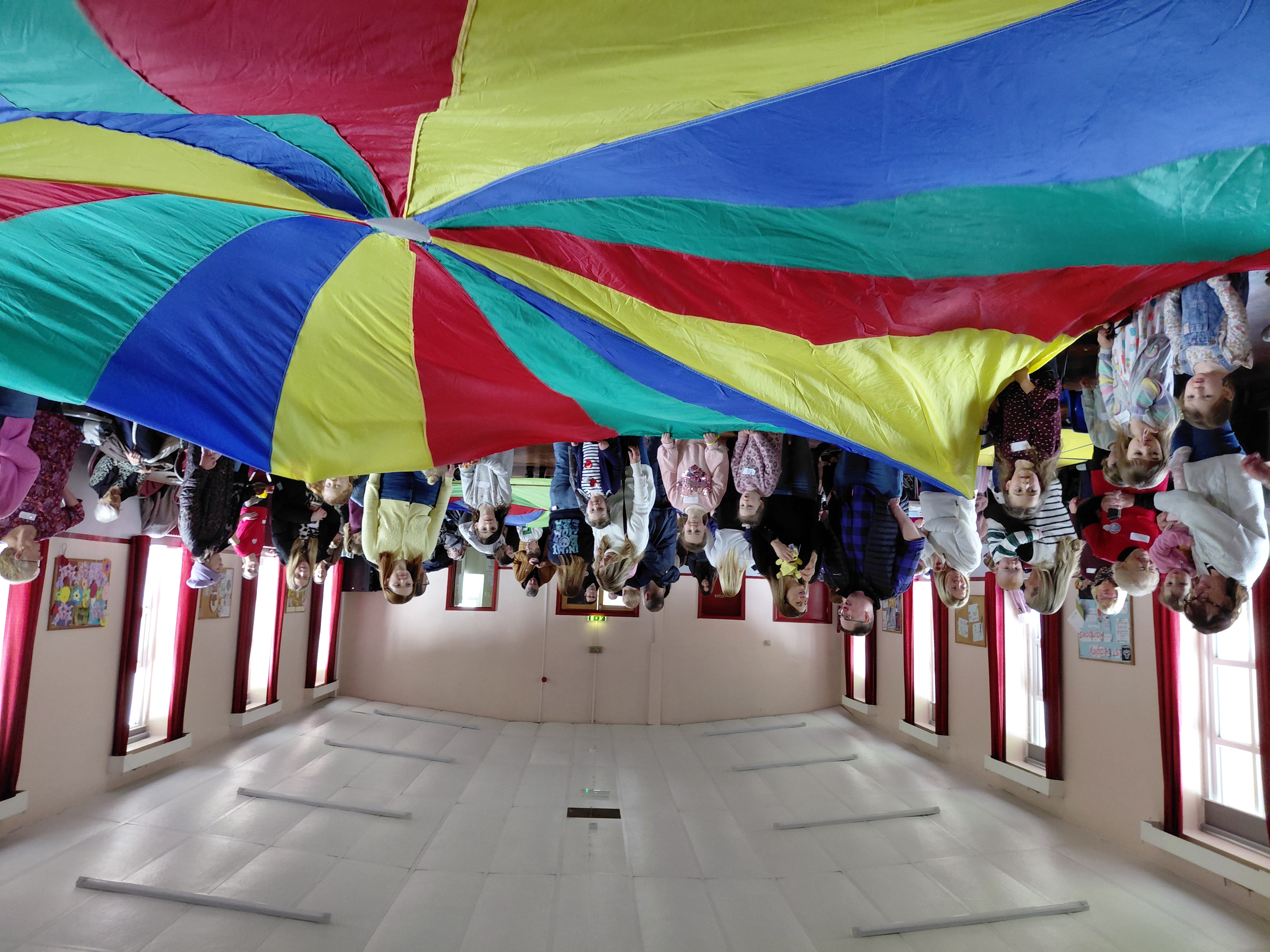 People around the side of a big multi-coloured parachute