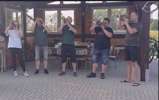 Five people standing in a garden room blowing traditional horns