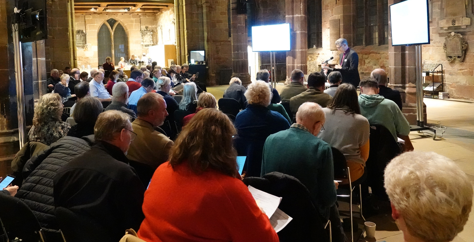 People sitting in a semi circle at diocesan synod in St Helen's church, taken from behind.