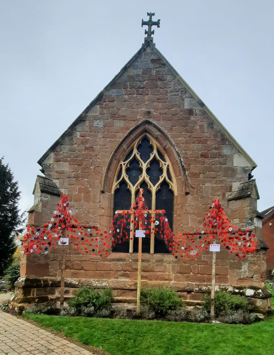 The end of St Peter's Church with three crosses in front draped in poppies