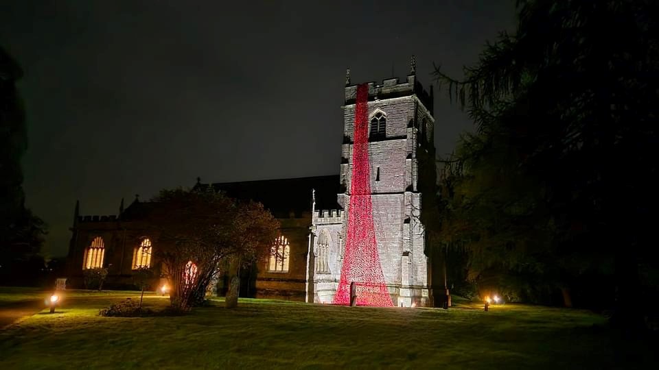 Inkberrow church at night with the cascade of poppies on the bell tower lit up