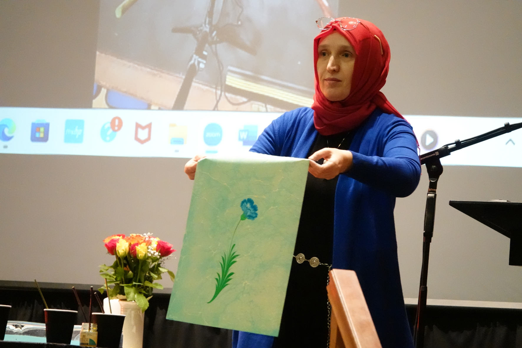 Muslim lady holds up a picture of a flower created using marble art