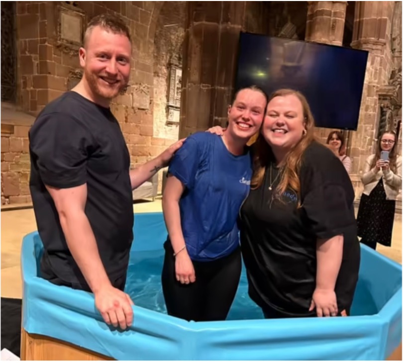 Young person standing in a font after full emersion baptism with the Revds Fraser Oates and Jess Fellows