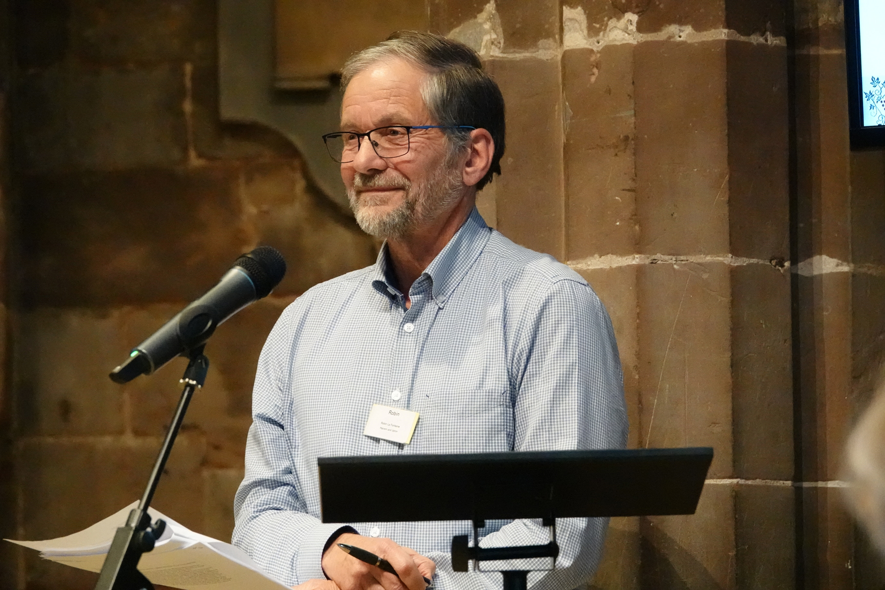 Robin La Fontain standing behind a microphone at diocesan synod