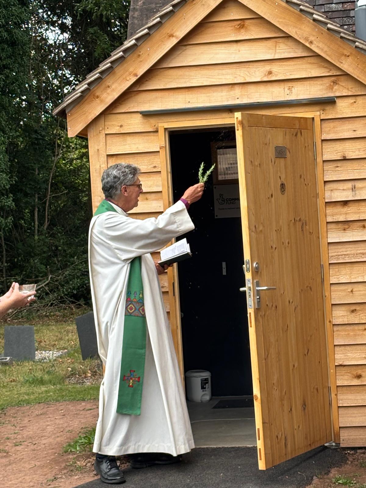 Bishop Martin sprinkling holy water on the new toilet building