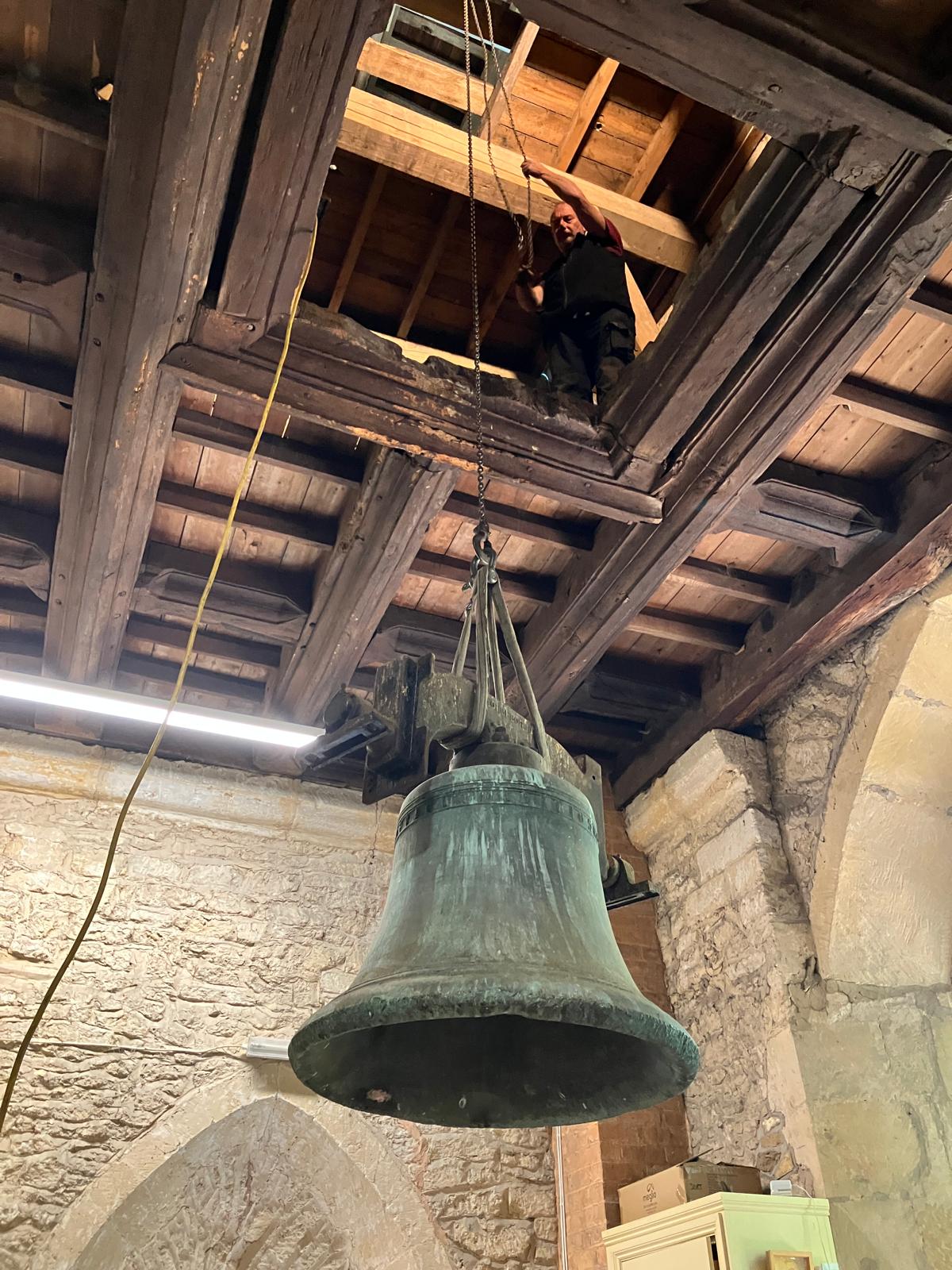 Bell being lowered on a rope through a square hole in the roof of Elmley Castle church