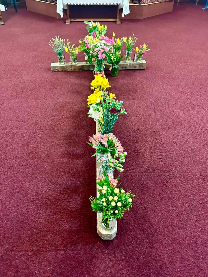 Jars of flowers positioned on a large wooden cross