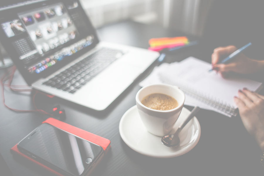 Laptop open with an online meeting happening. A cup of tea and hands writing in a notebook.