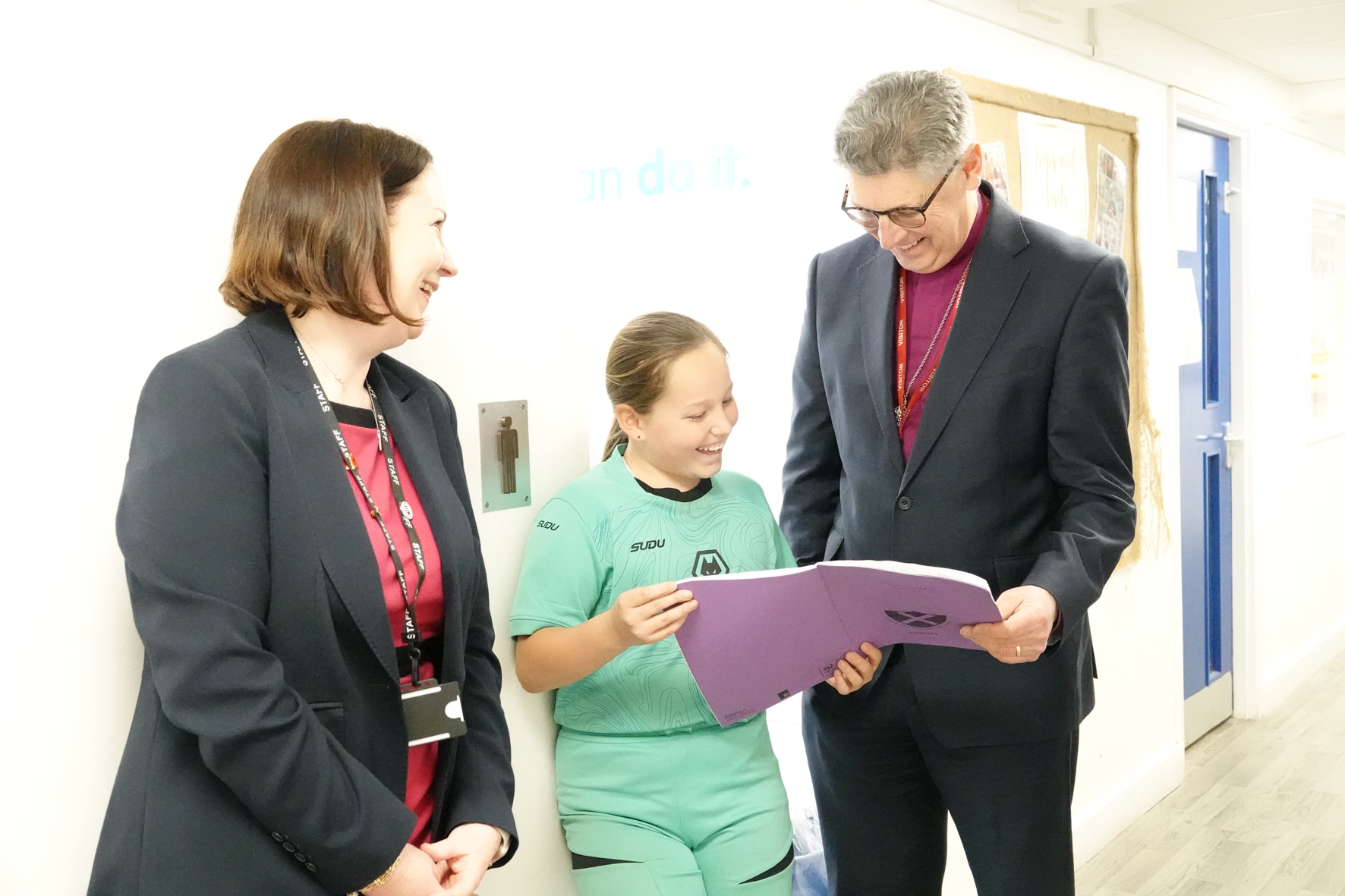 Bishop Martin looks at a school book with a young girl while the CEO of DoWMAT looks on