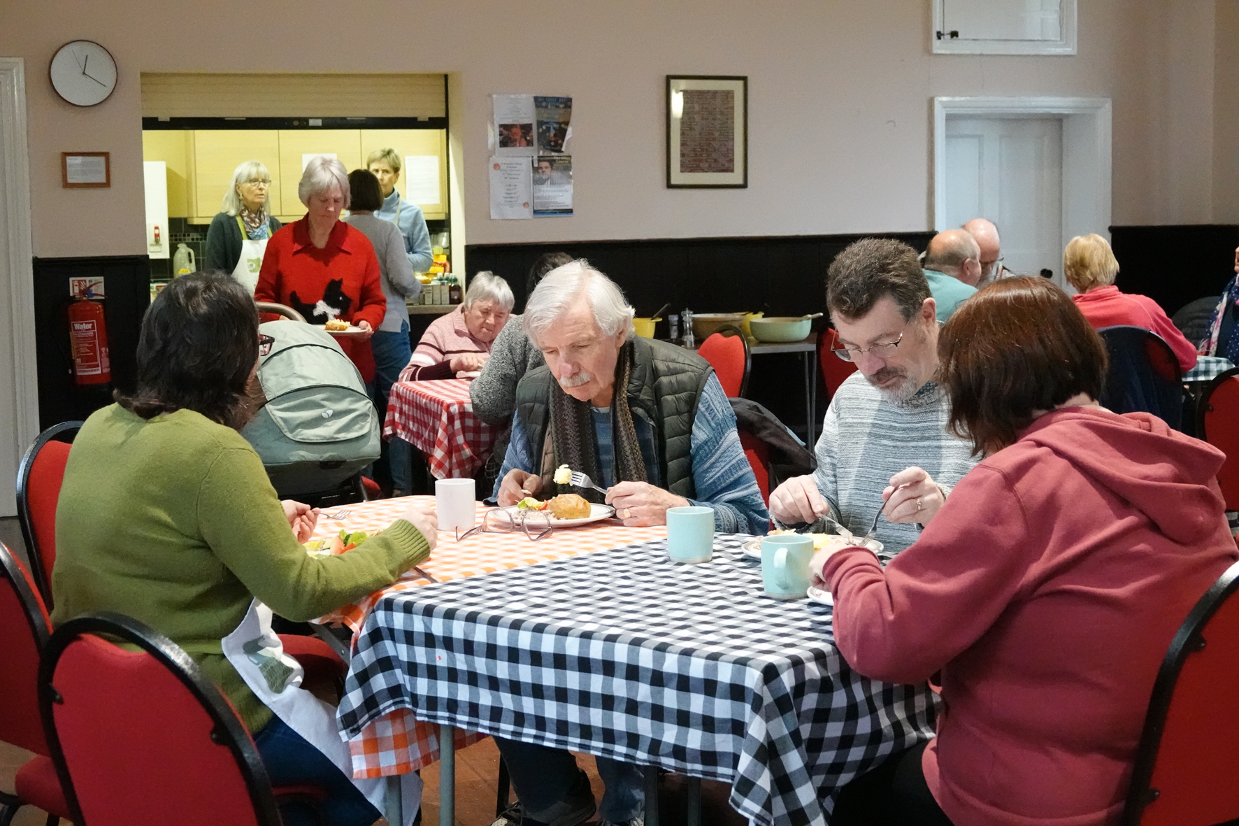 People sitting at tables in a village hall eating lunch