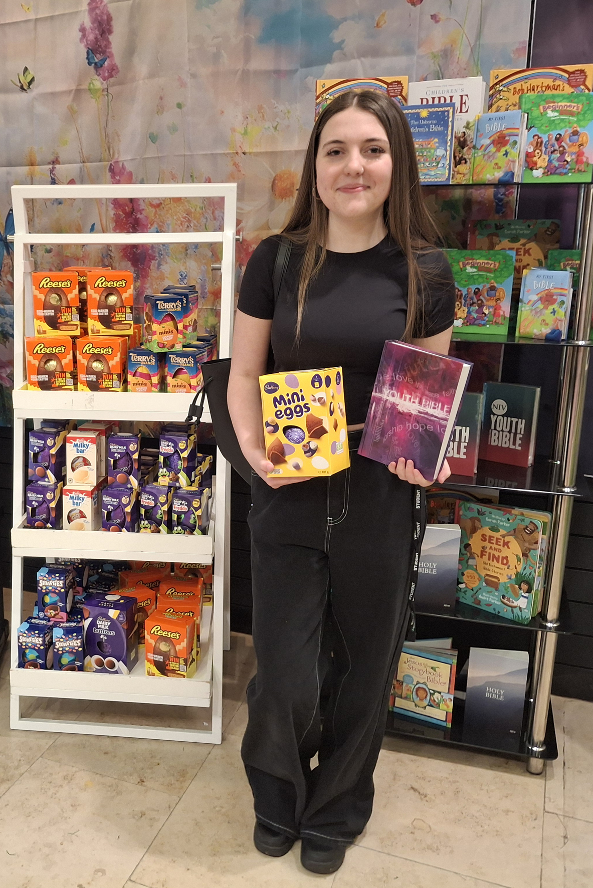 A teenage girl holding a bible and an Easter egg standing in front of a display