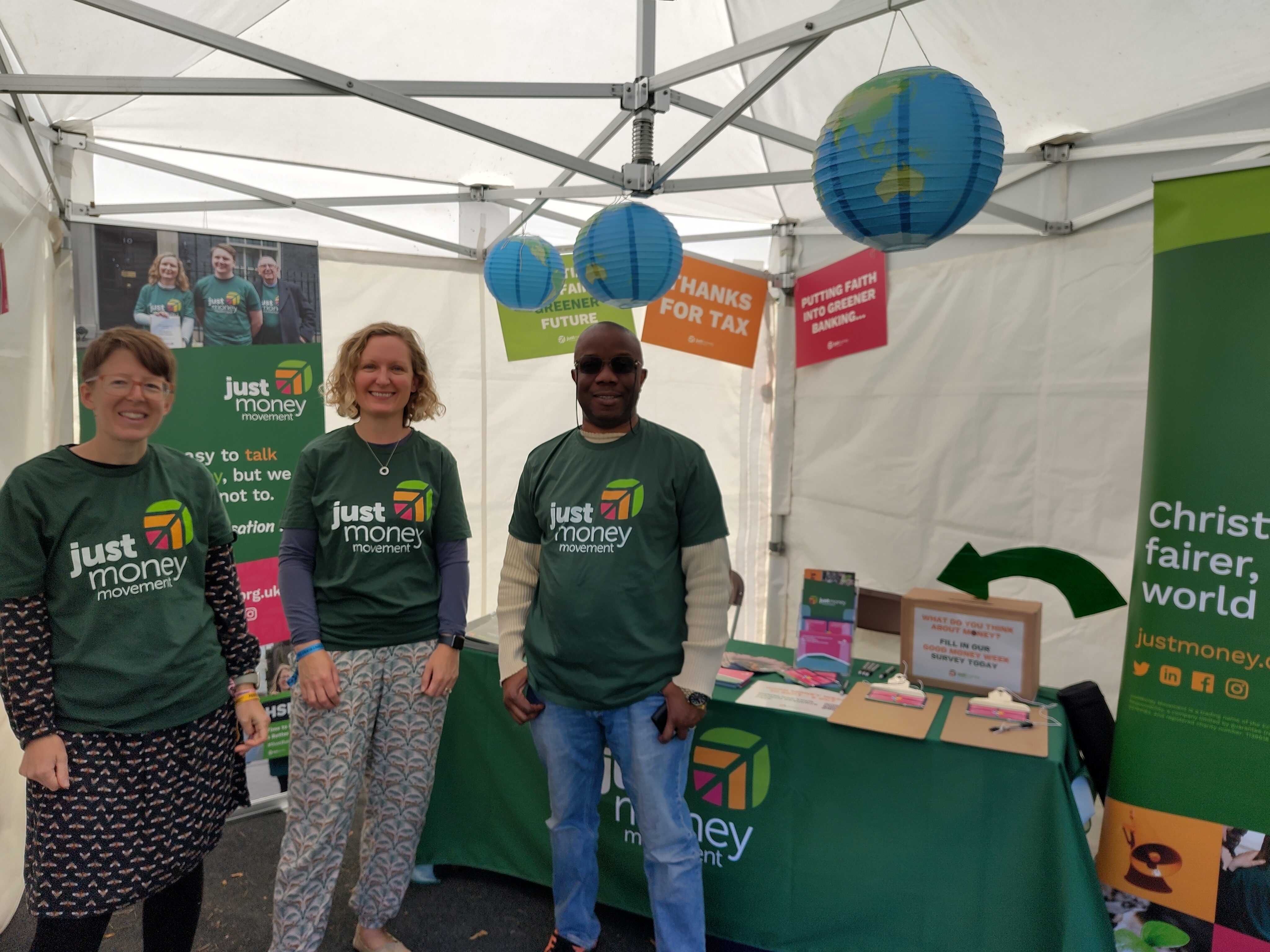 Three people in JustMoney t-shirts standing in a tent featuring the JustMoney stall