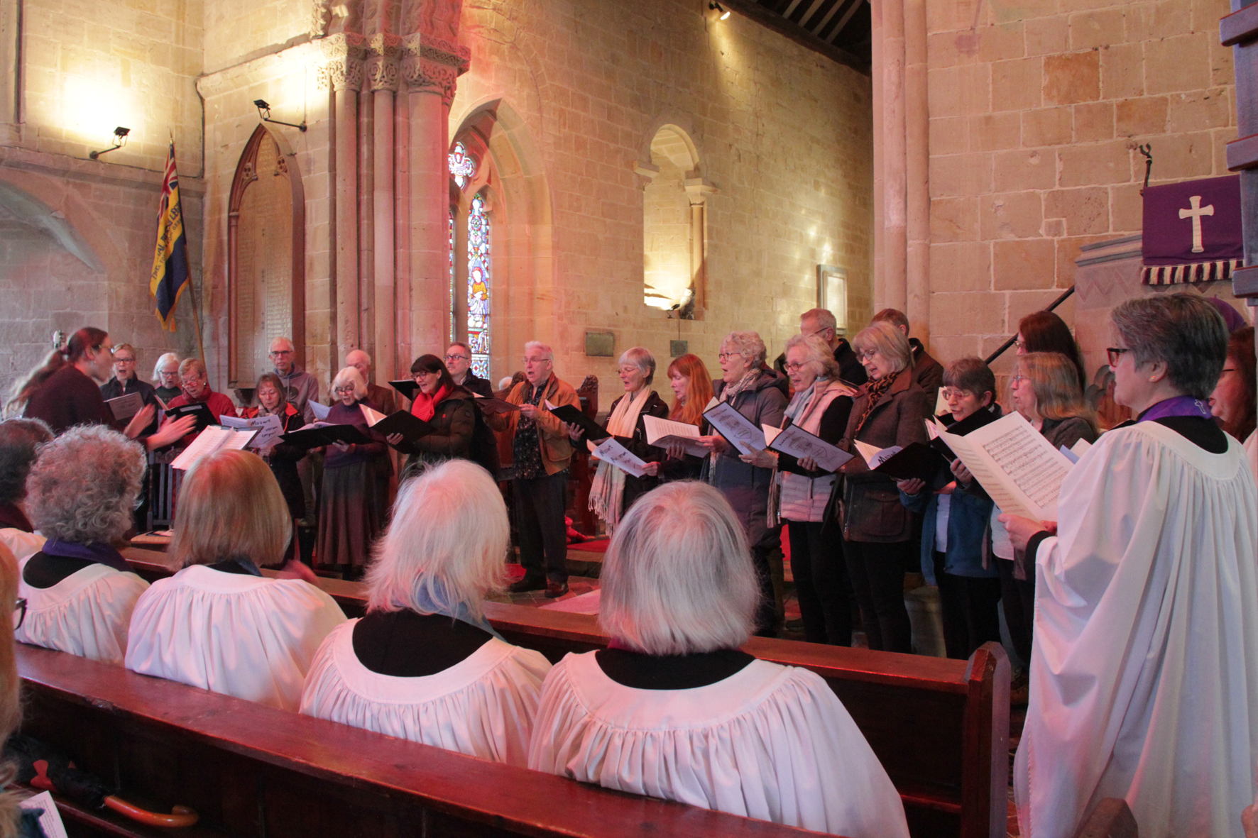 Members of the combined choir standing at the front of Rock Church while a row of people in robes watch