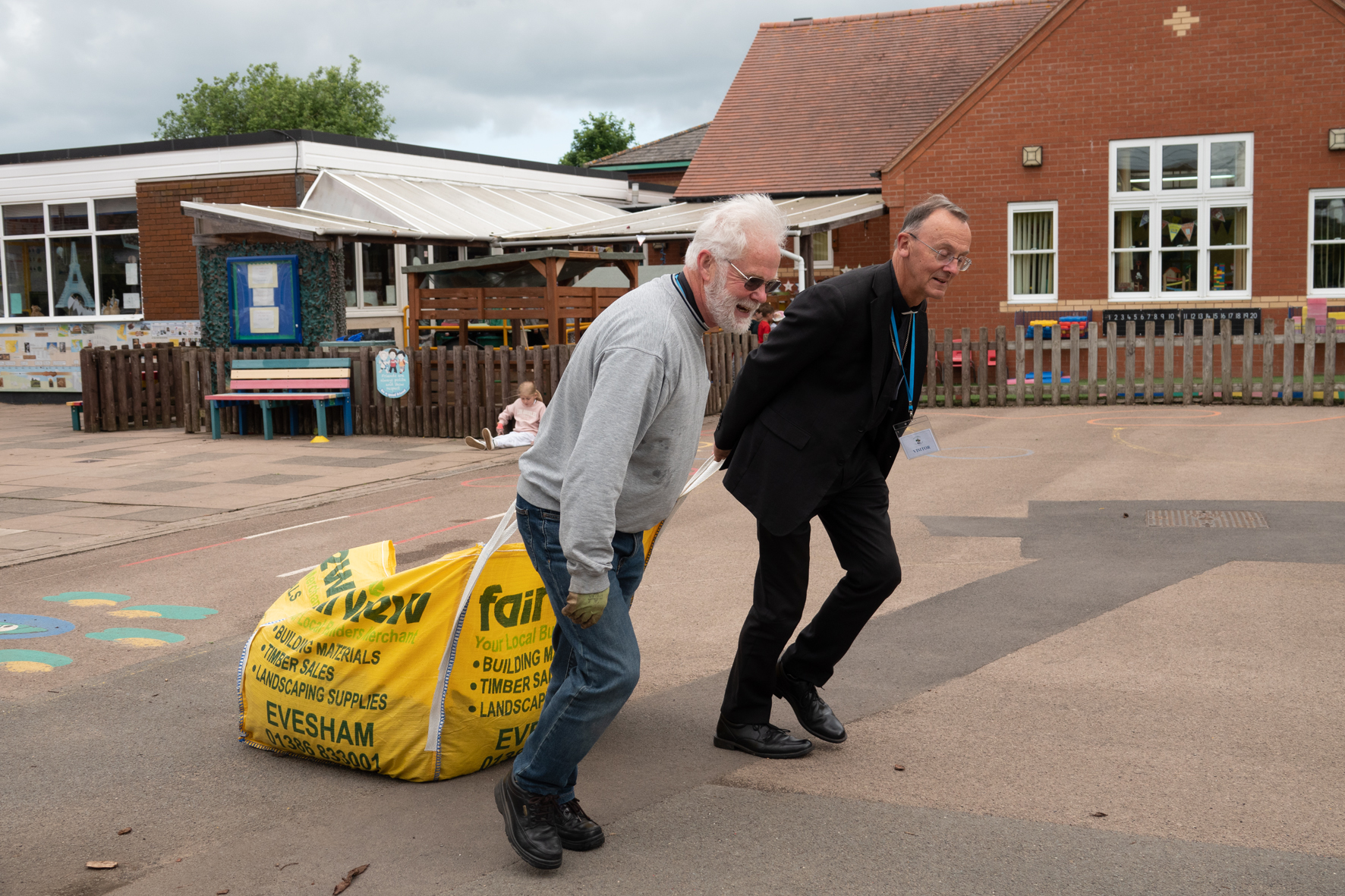 Bishop John and Richard Thorniley drag a bag of bark chippings at Harvington School
