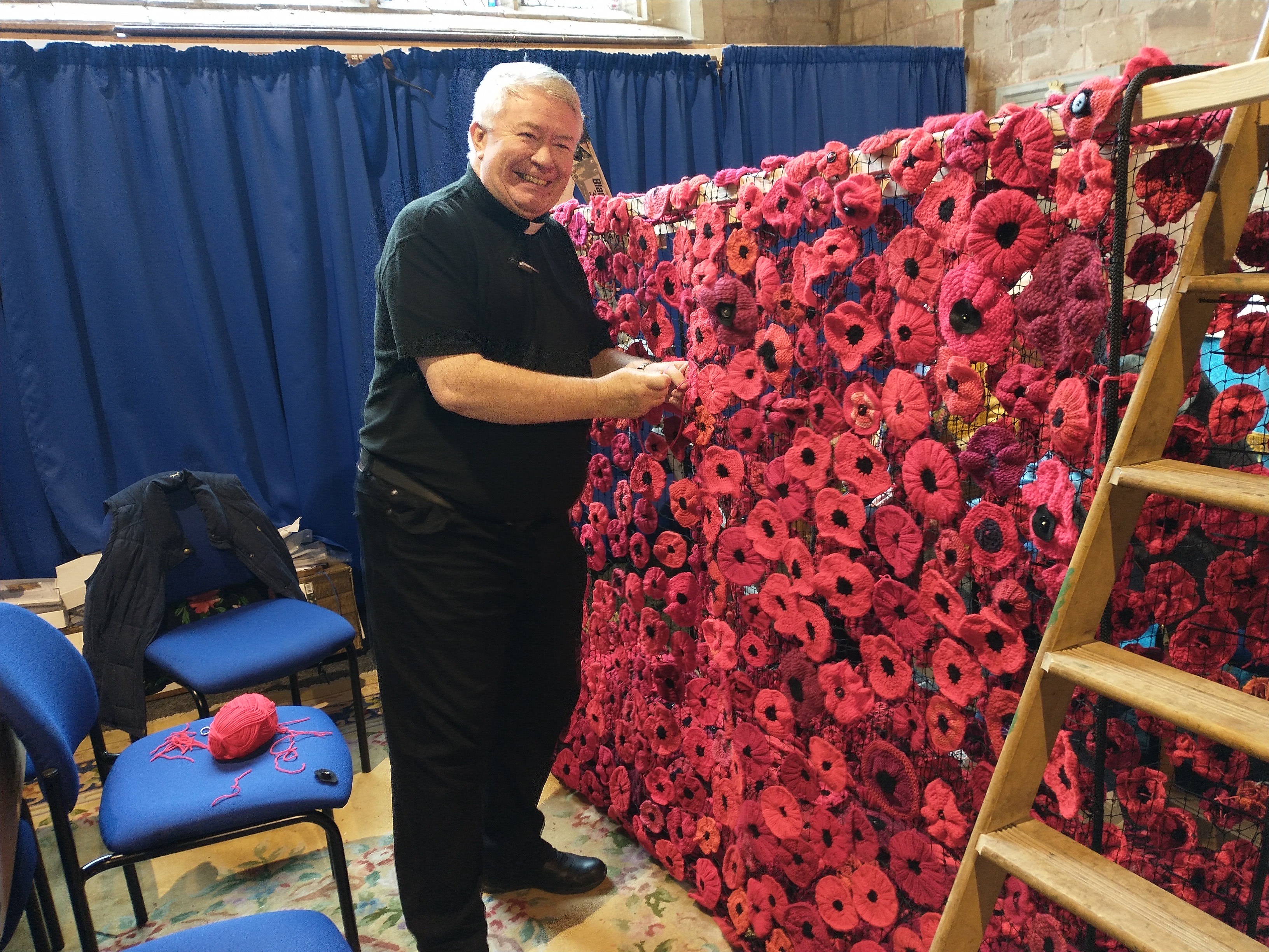Gary Crellin stands next to a draped net of poppies sewing one on.