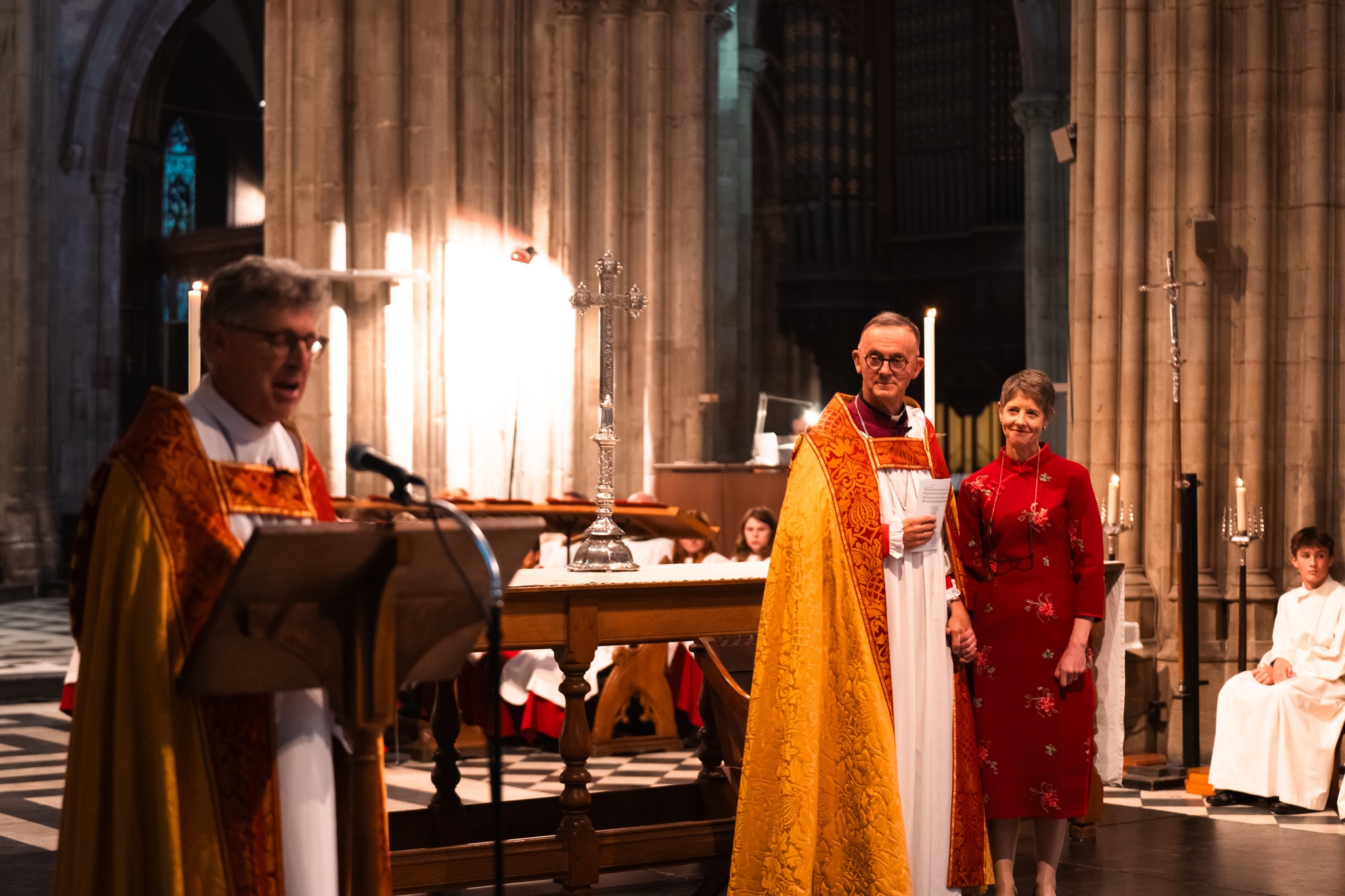 Bishop John and HJ standing in front of the altar with Bishop Martin speaking at the lecturn