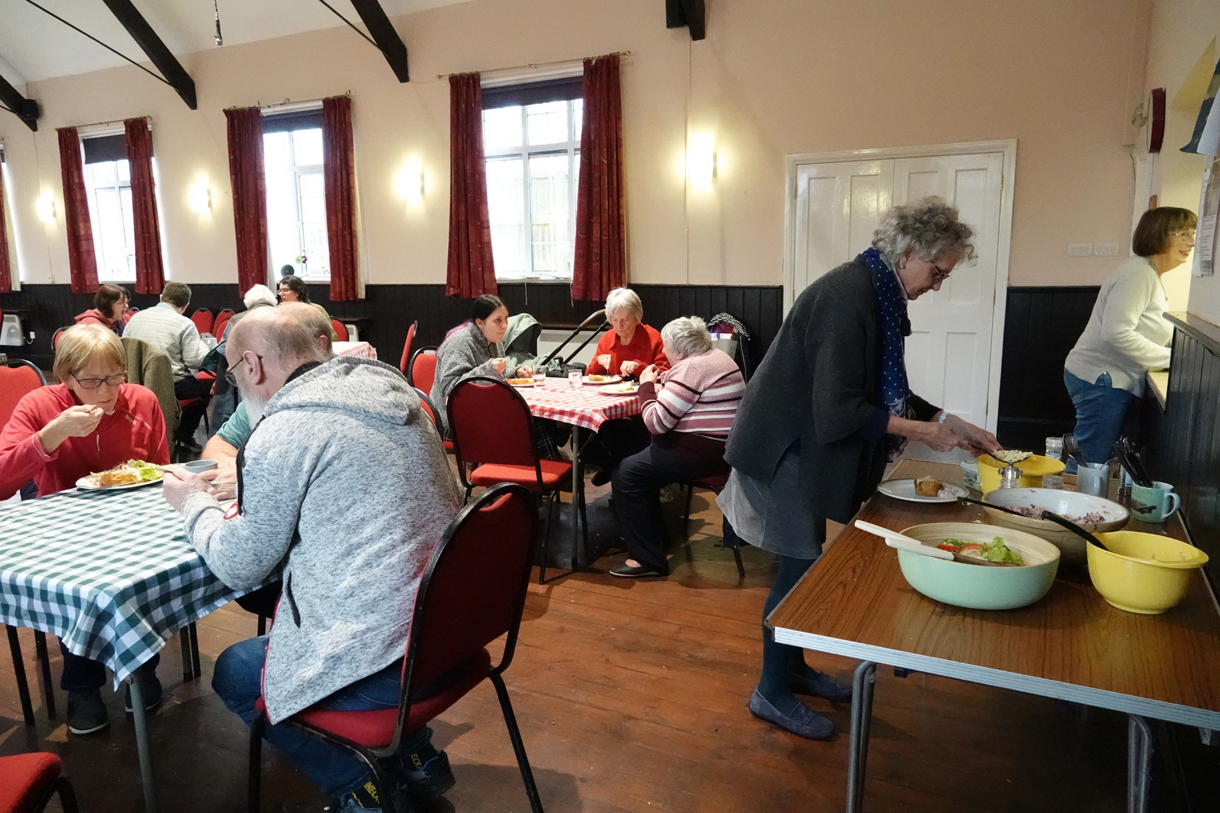 People sitting at tables eating lunch while someone puts food from their plate from a serving table