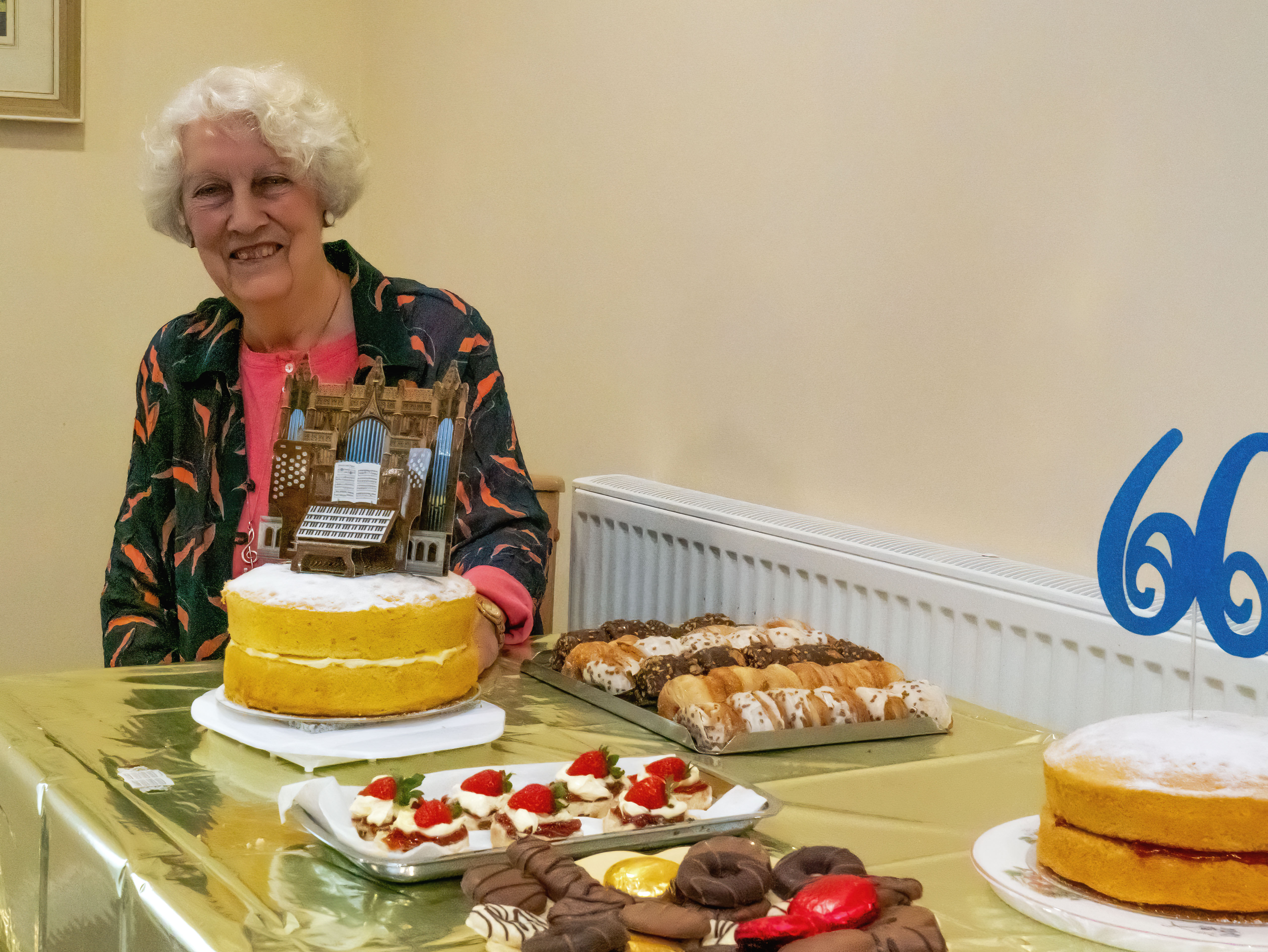 Lady sat behind the refreshments with two cakes - one with 66 on and one with a cardboard pop up organ on the top