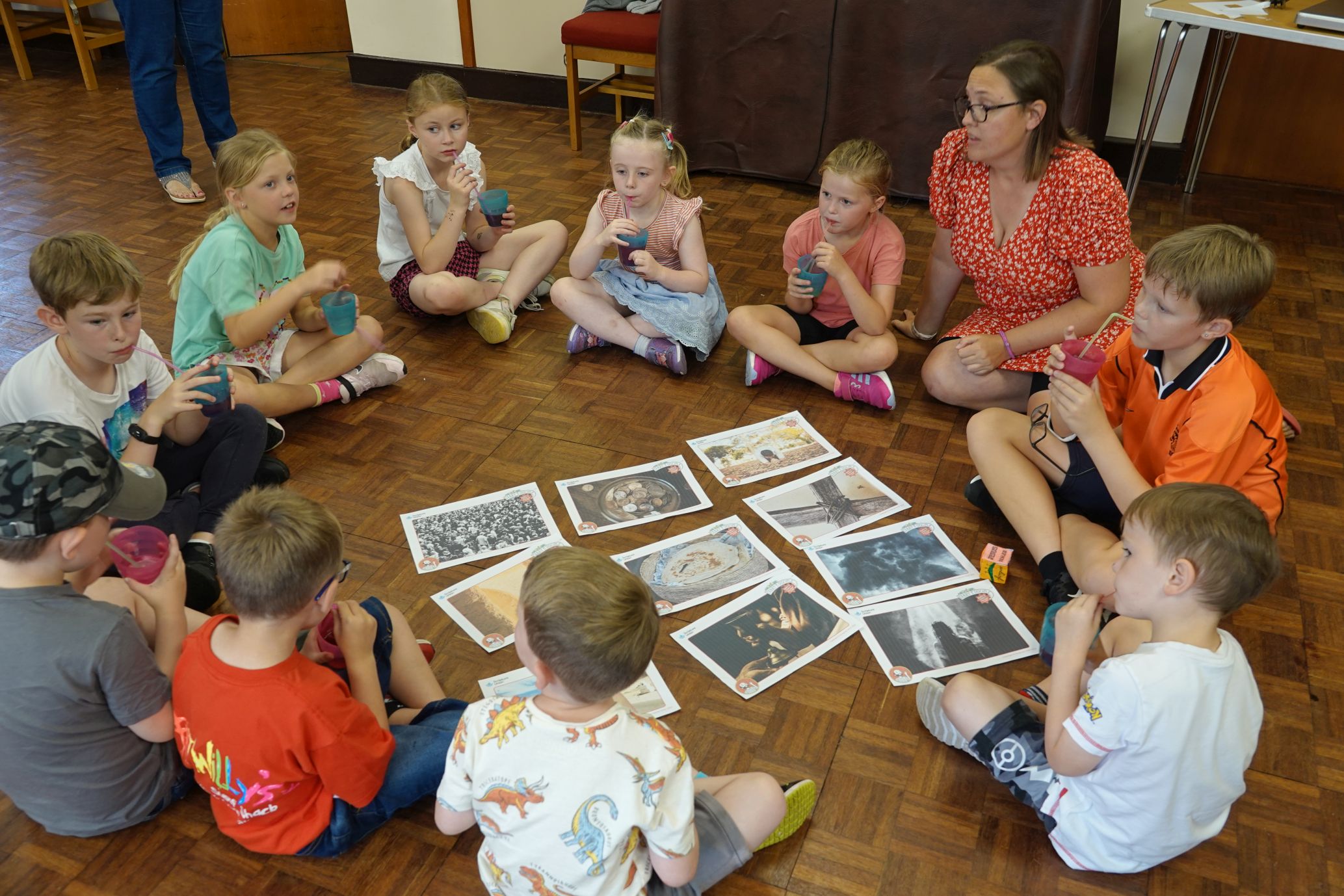 Children and Youth worker Sian Morgan sits on the floor in a circle with the children discussing images in front of them in the centre of circle which relate to the video they watched earlier 