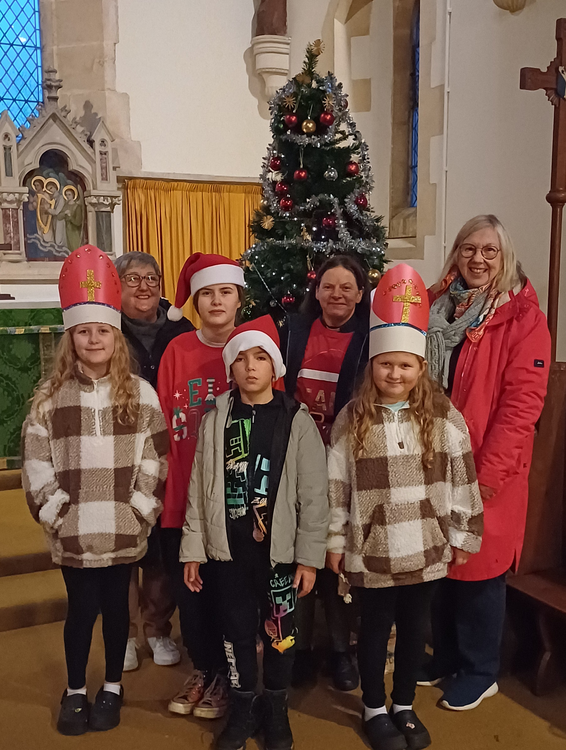 Children in Mitres and Santa haps next to the Christmas tree in St Nicholas' Church, Middle Littleton