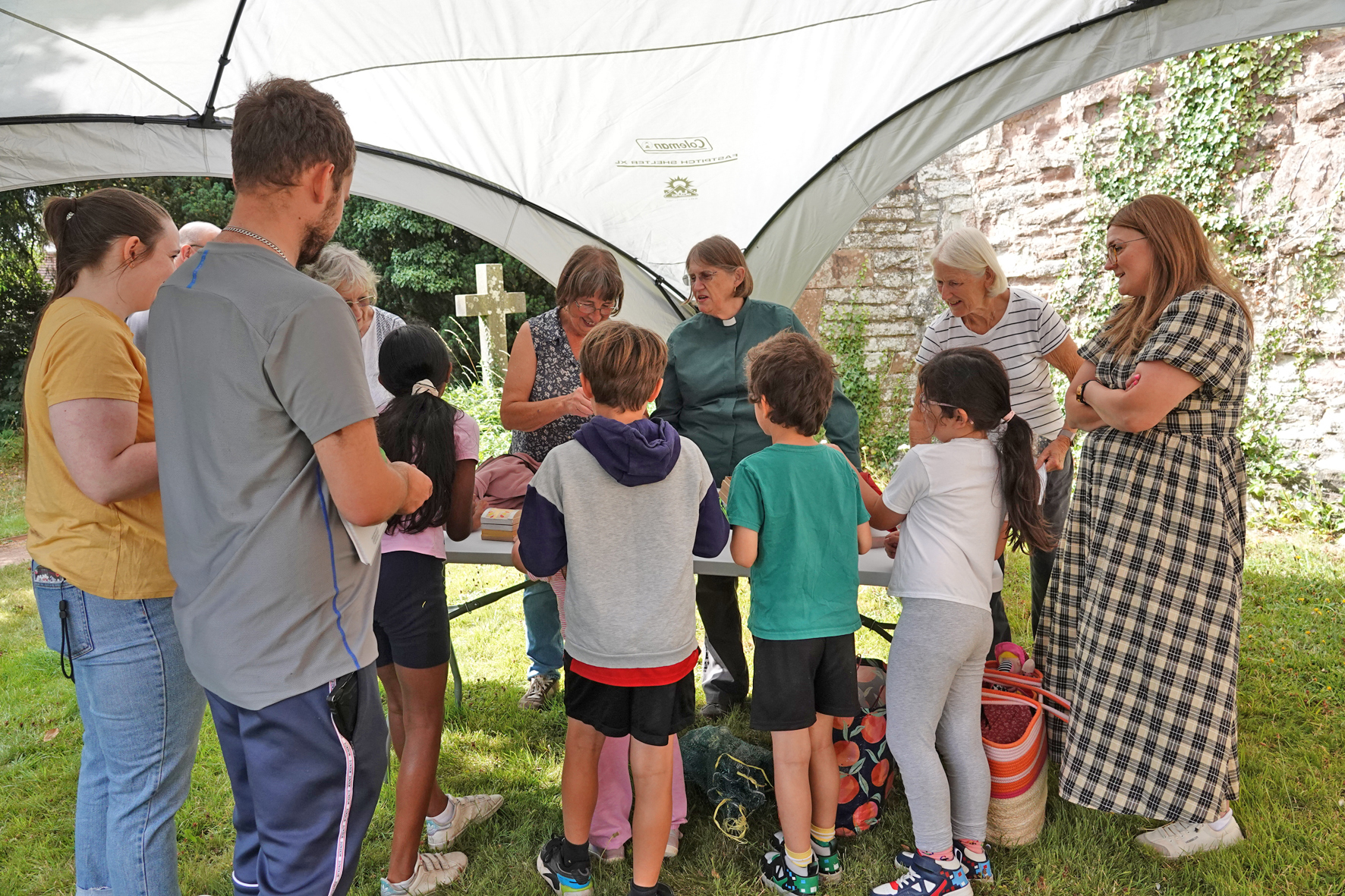 People of all ages gathered around a table under a gazebo outside the church