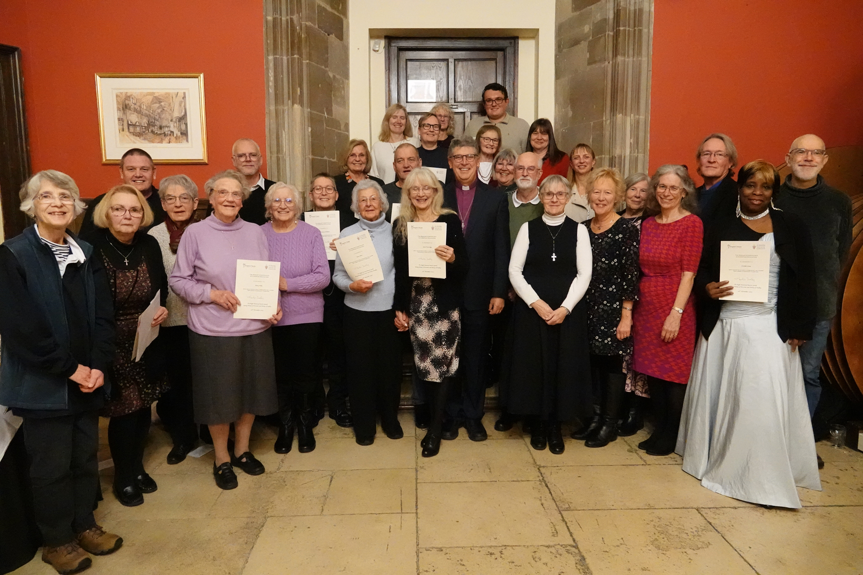 A group of people who have just received their Bishop's Certificate standing in a group on some stepswith Bishop Martin