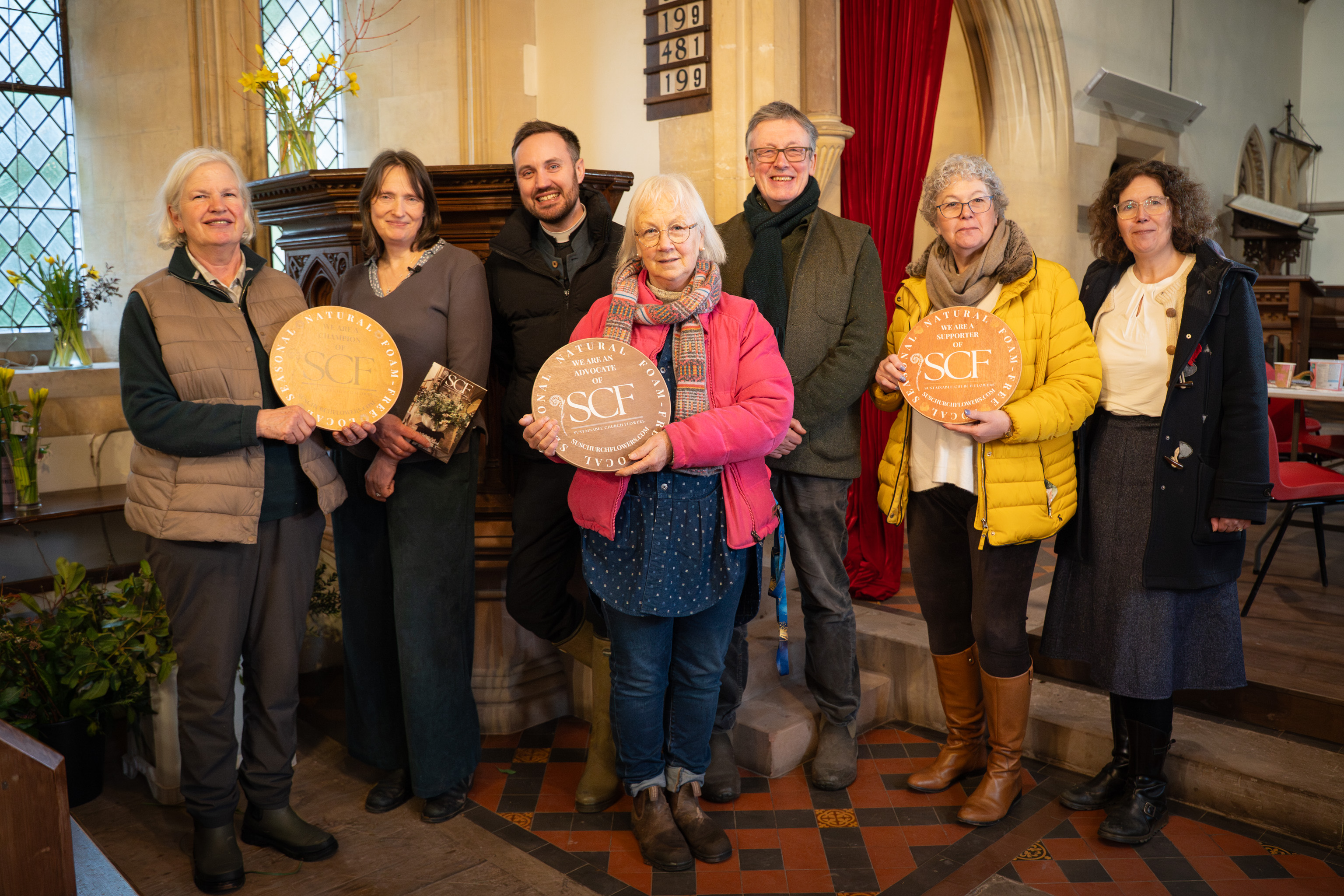 A group of people from the sustainable church flowers movement in a church holding SCF plaques