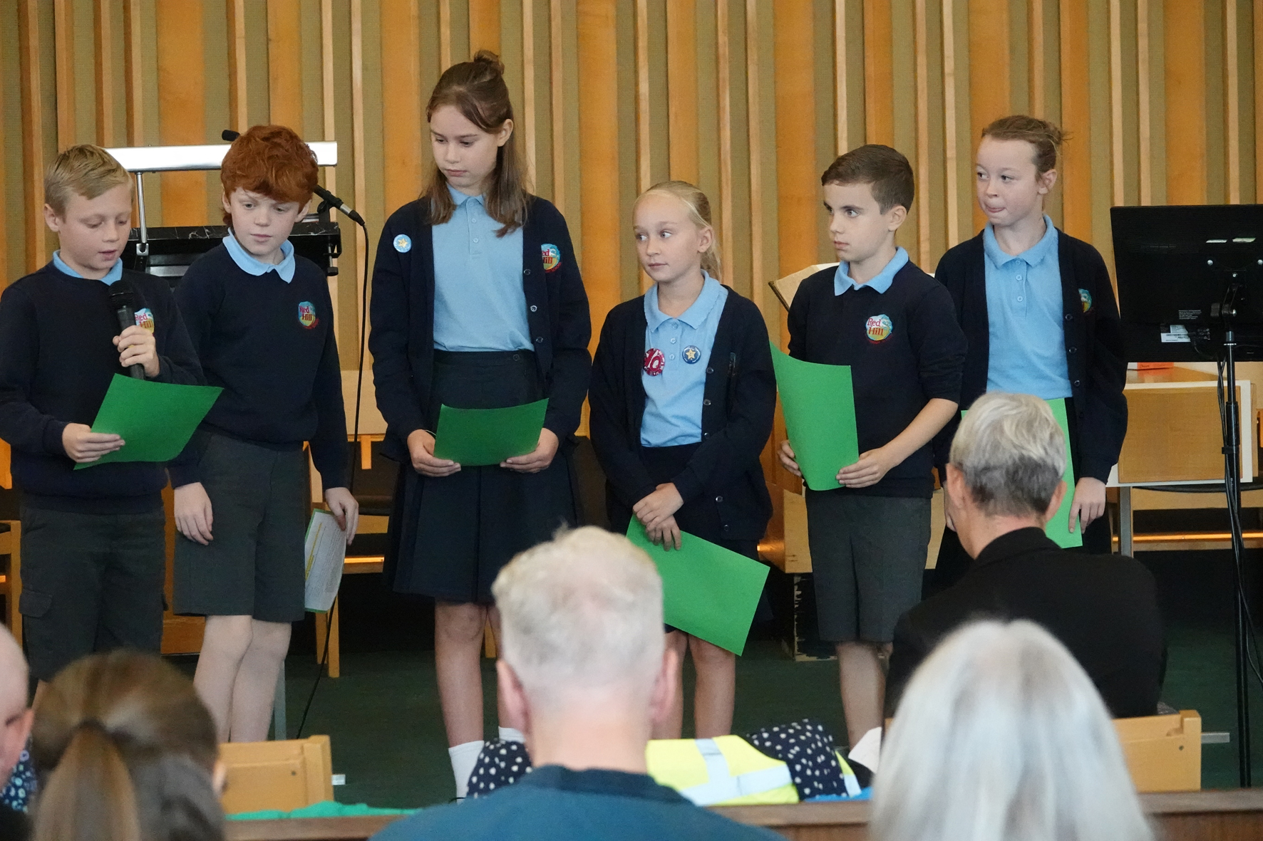 A row of children standing on a stage reading prayers