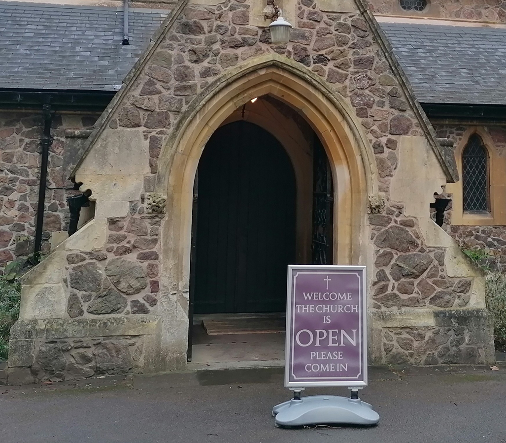 A church door with an 'open' sign in front of it.