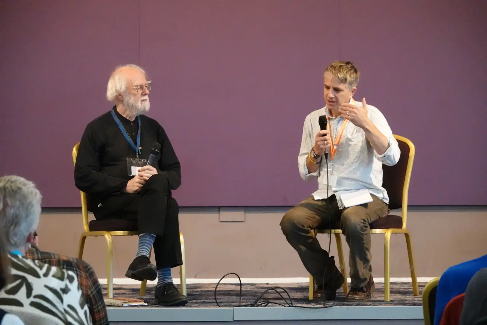 Bishop Hugh speaking into a microphone as he sits on a stage interviewing Rowan Williams
