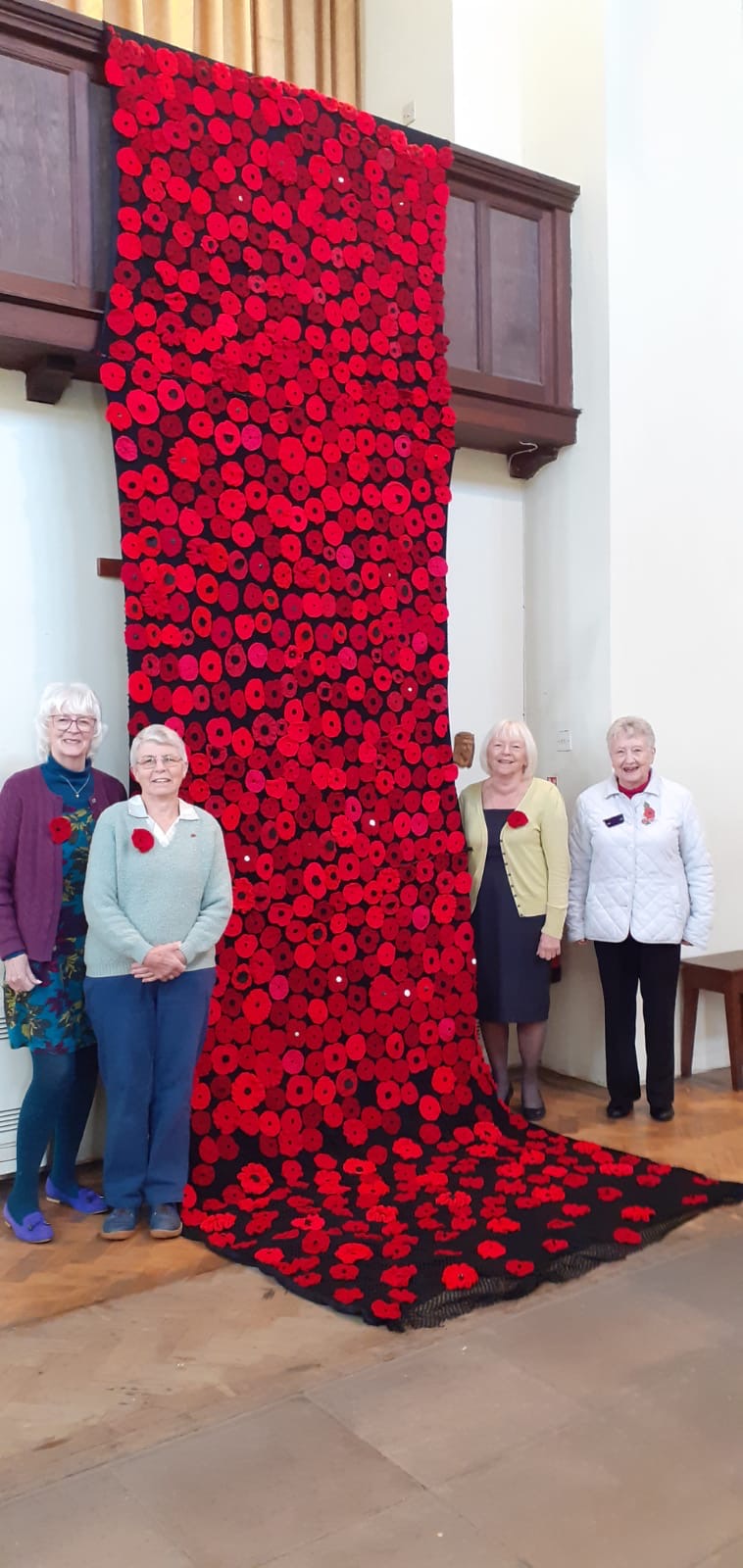 Poppies cascading from the organ loft to the floor in Holy Innocents' Church with 4 people standing next to it. 