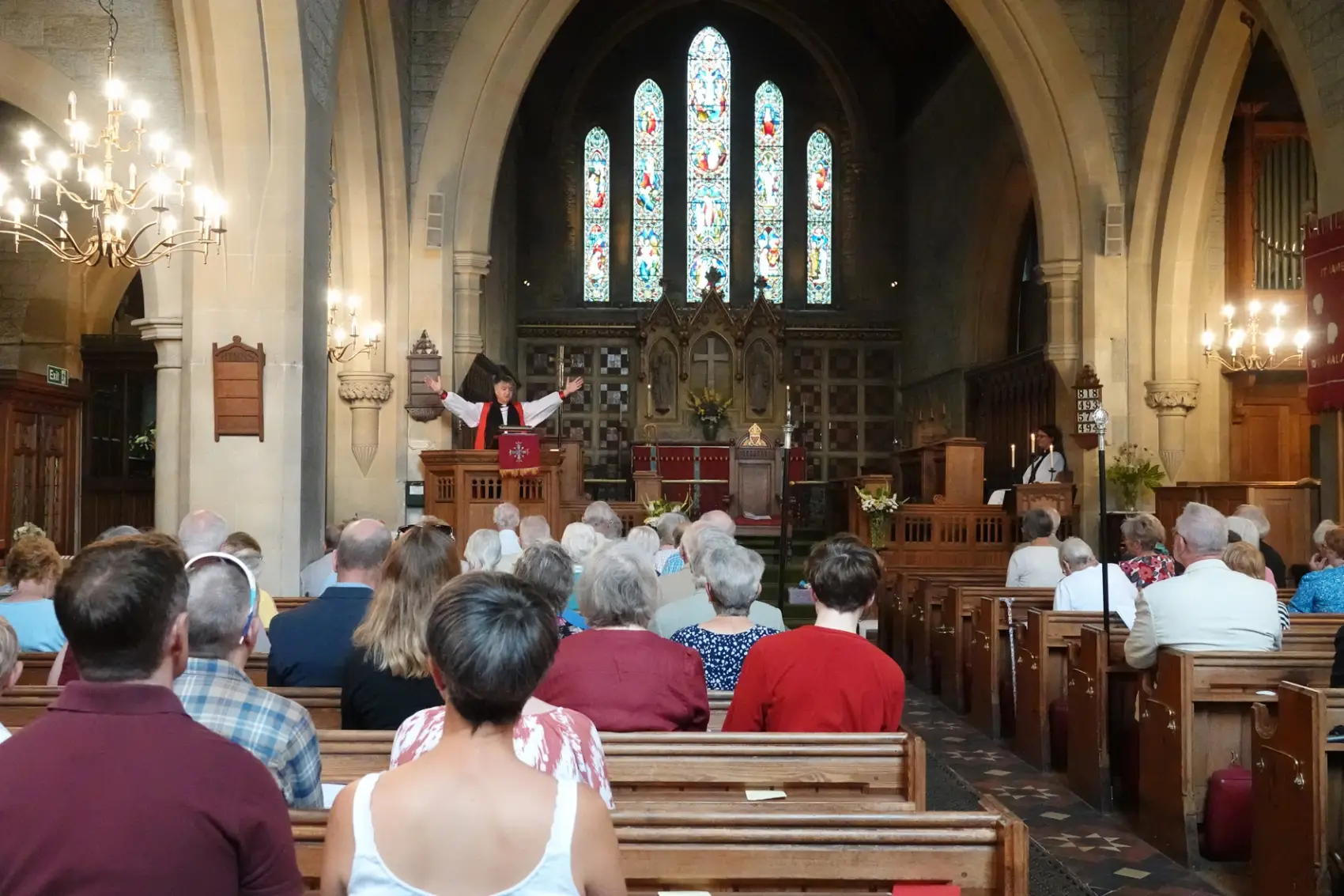 Bishop Hugh in the pulpit of St James Church with his arms wide open with people sitting in the pews listening to him