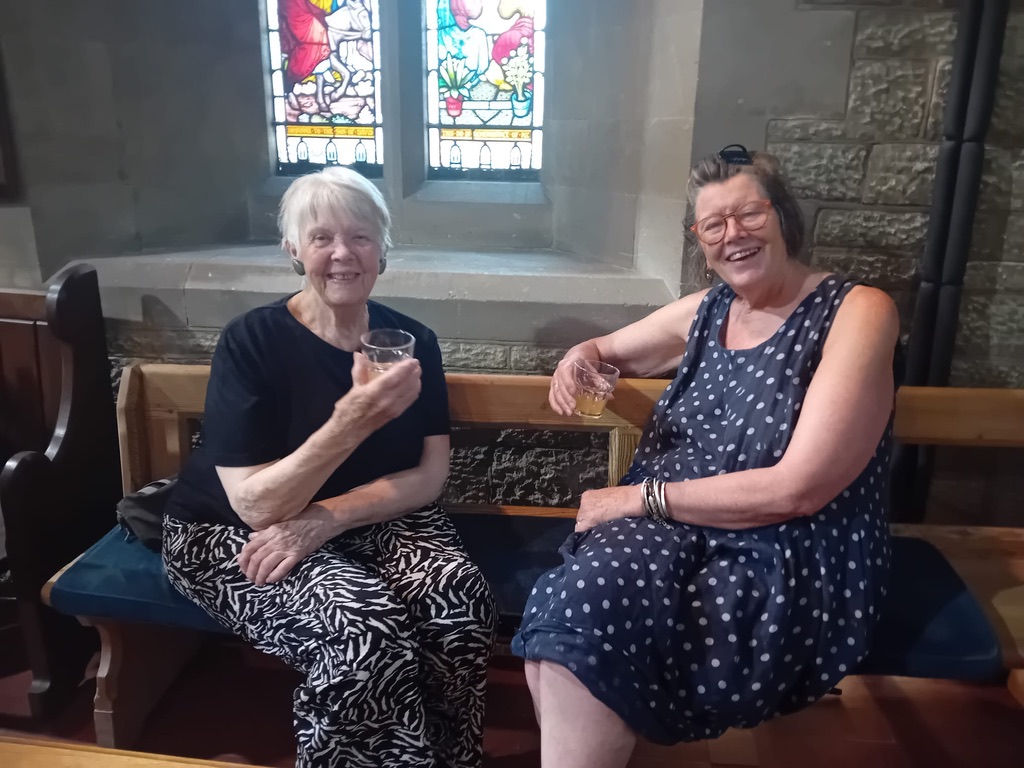 Two ladies enjoy a cold drink as they sit on a pew in St Peter's Church