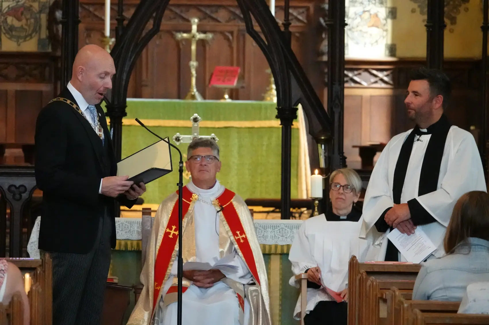 Deputy Mayor of Dudley speaking into a microphone to Chris Smith at the front of church as the Bishop of dudley sits behind