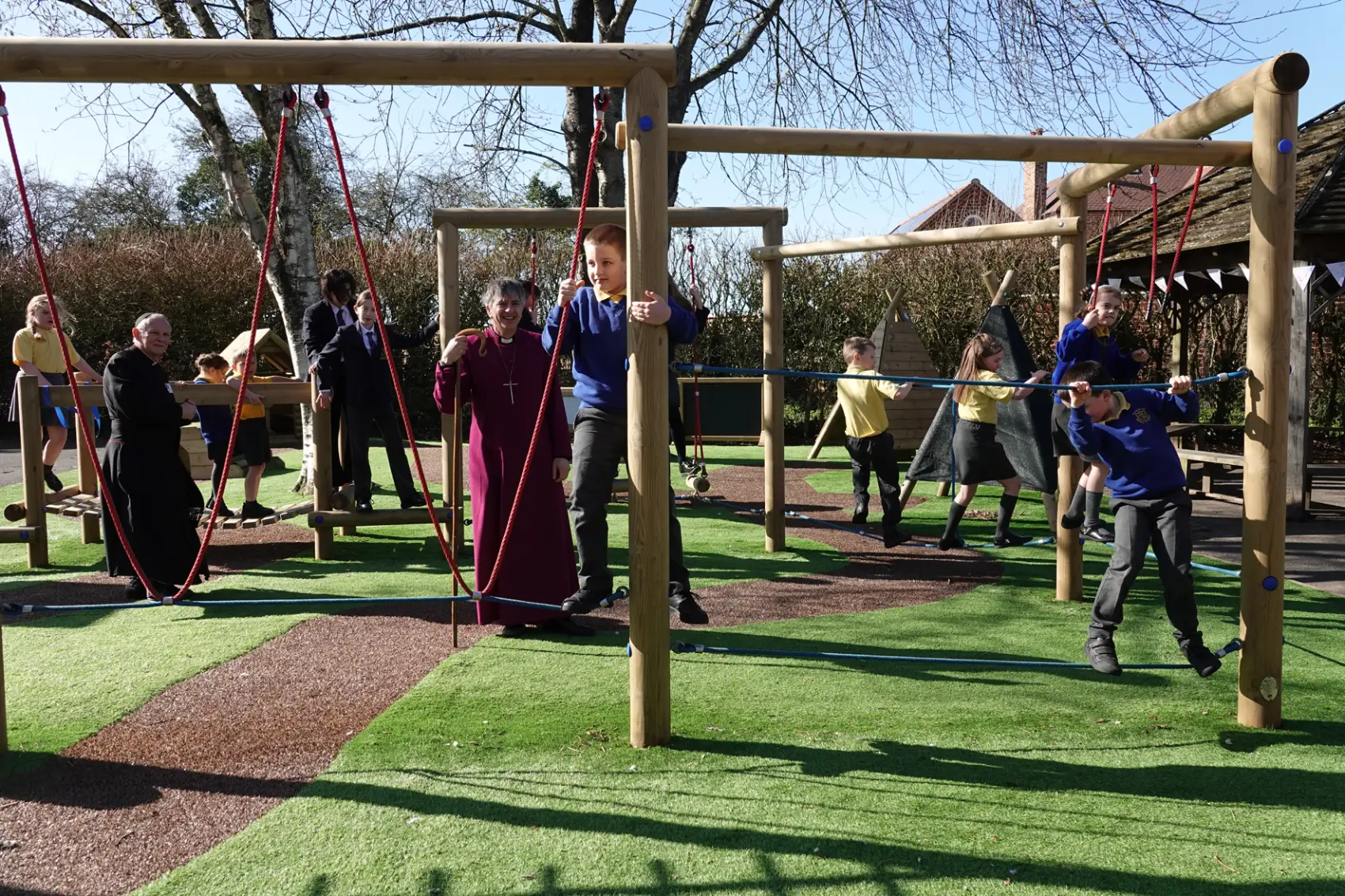 Bishop Hugh standing in the middle of a set of wooden play equipment while children climb around him.
