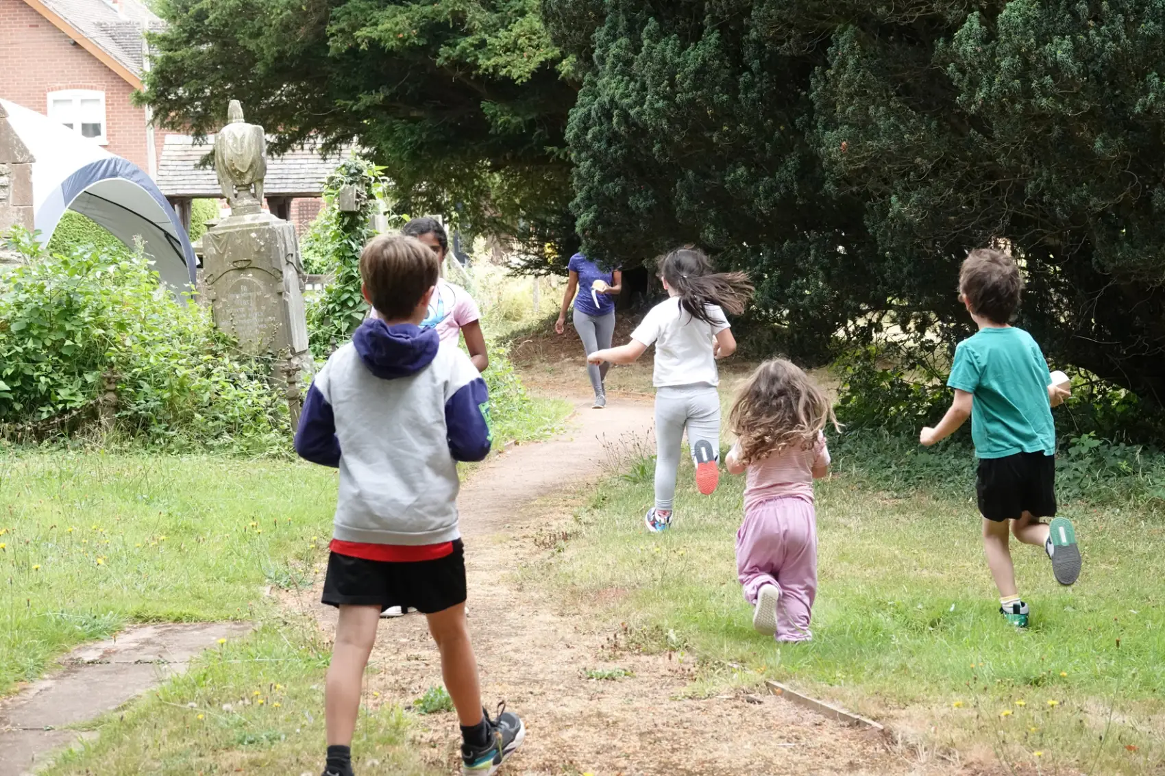 Children run down the path away from the camera at Clifton on Teme churchyard