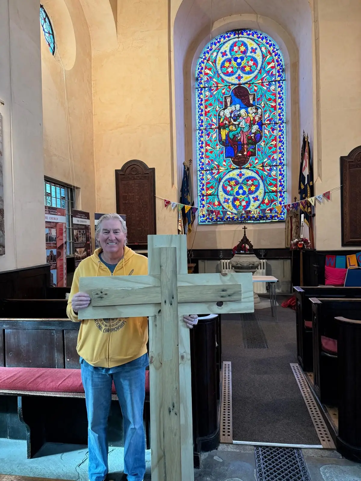 A man holding a big plain wooden cross at the front of church